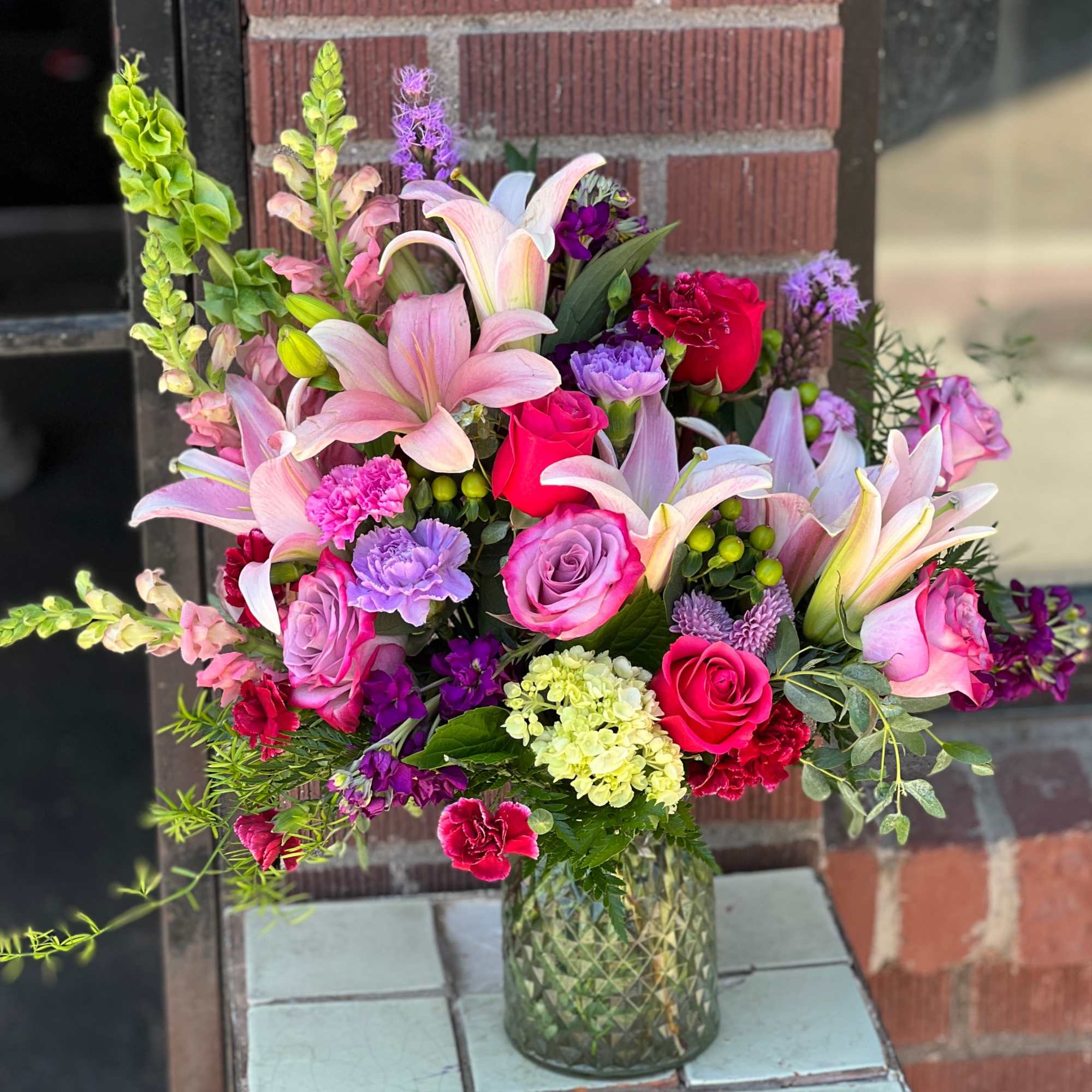 Mixed bouquet of pink lilies, roses, and carnations in a glass vase