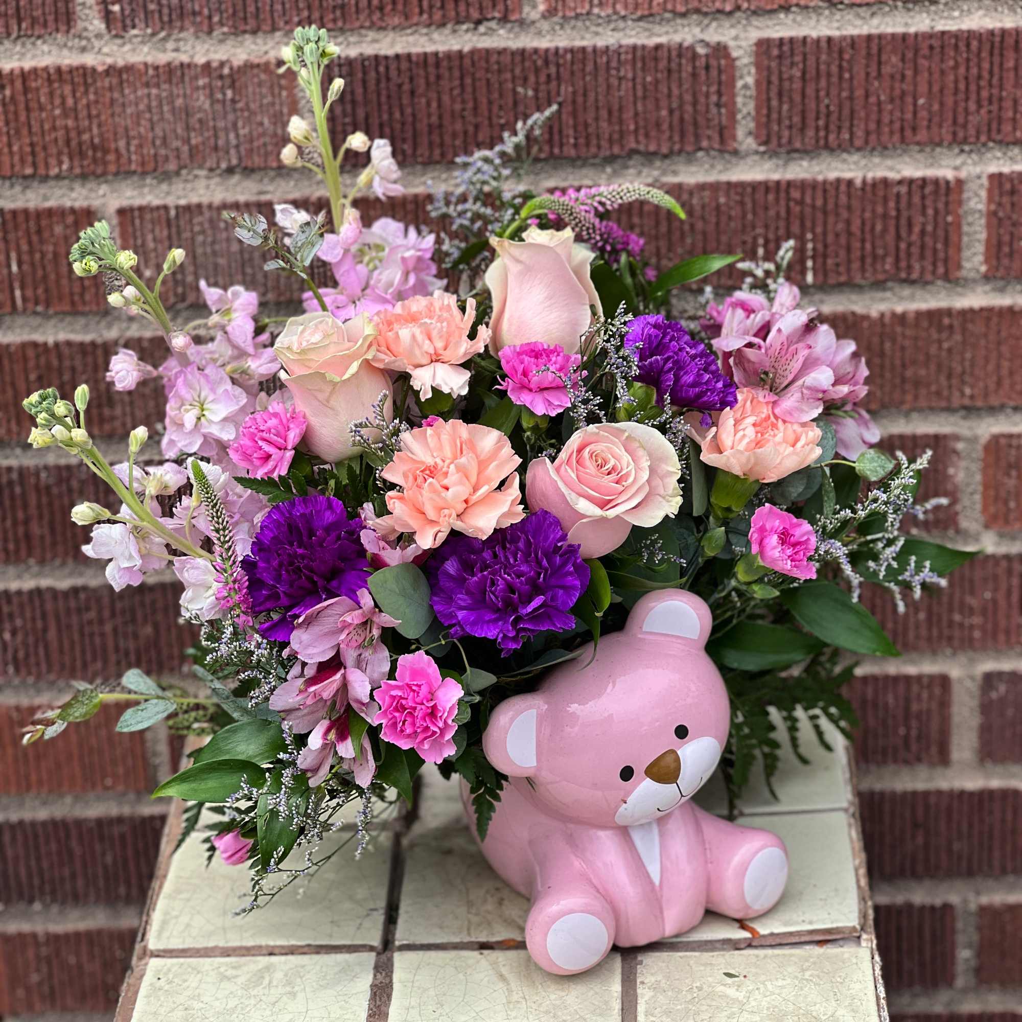 Pink and purple flower arrangement with a pink teddy bear figurine