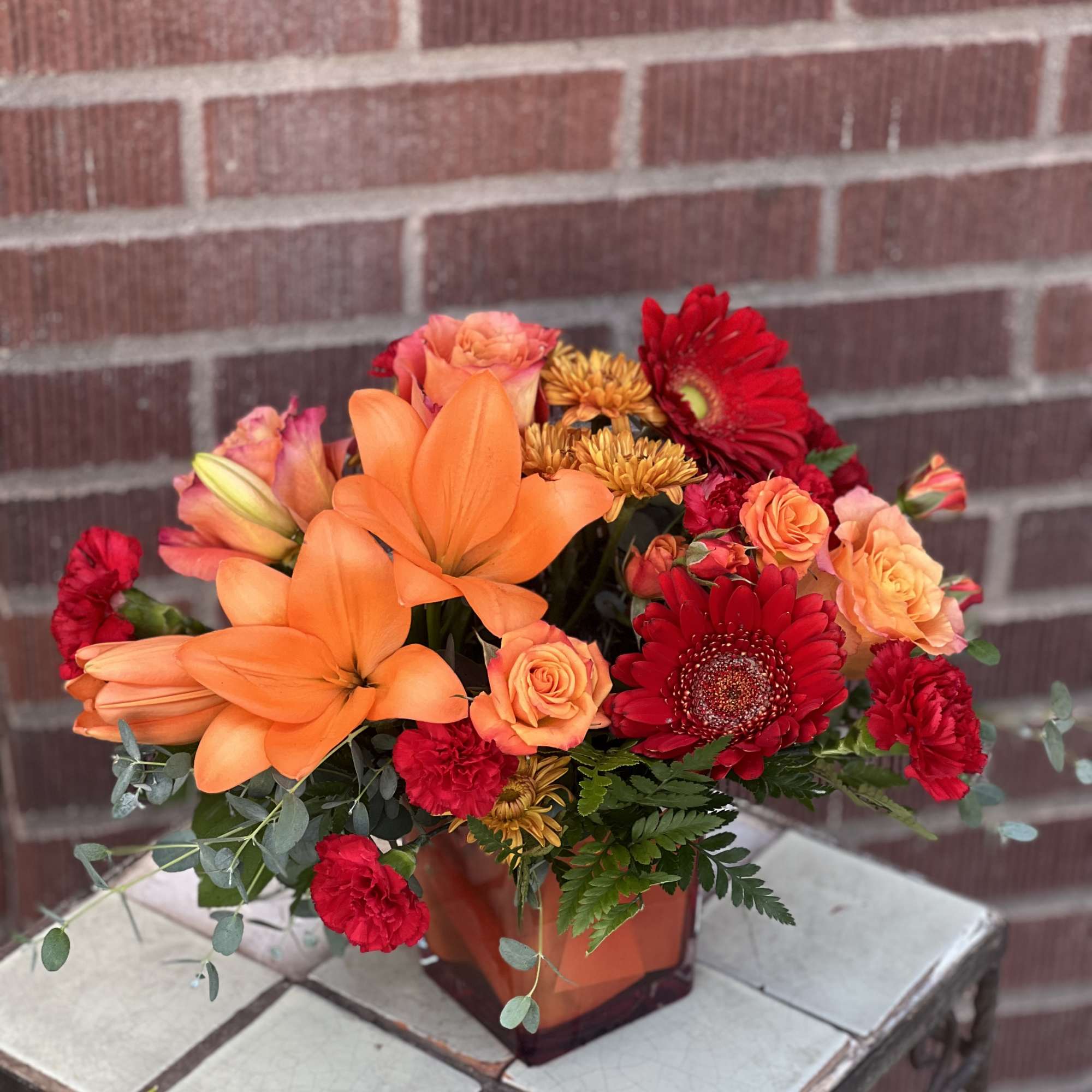 Orange lilies and red gerbera daisies in a square vase