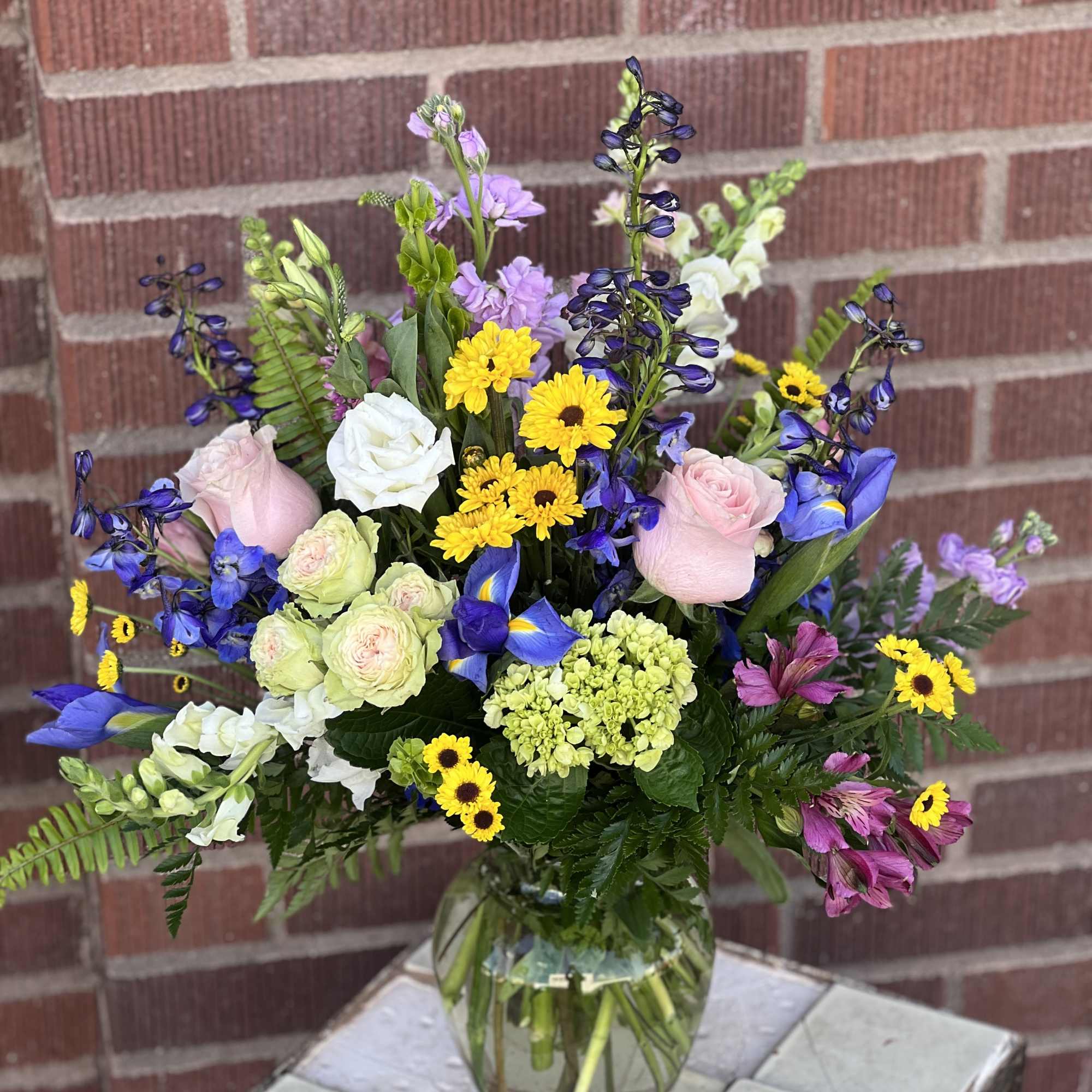 Mixed bouquet in a clear glass vase with pink, white, yellow, and blue flowers