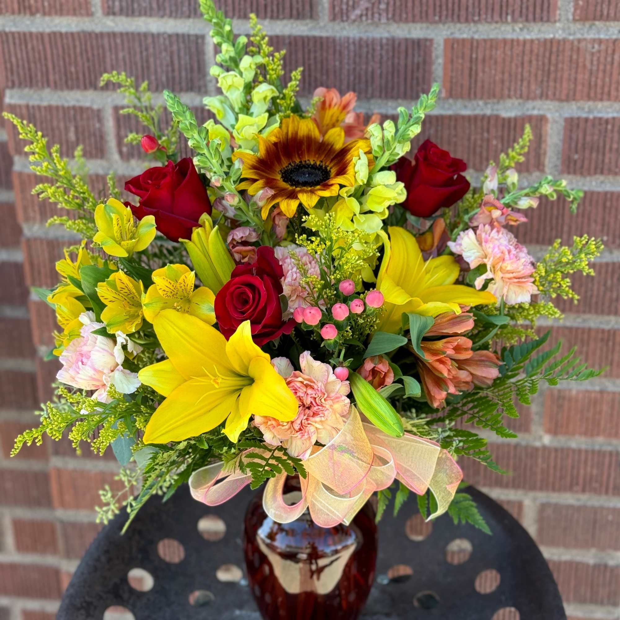 Mixed bouquet of yellow lilies, red roses, and a sunflower in a vase