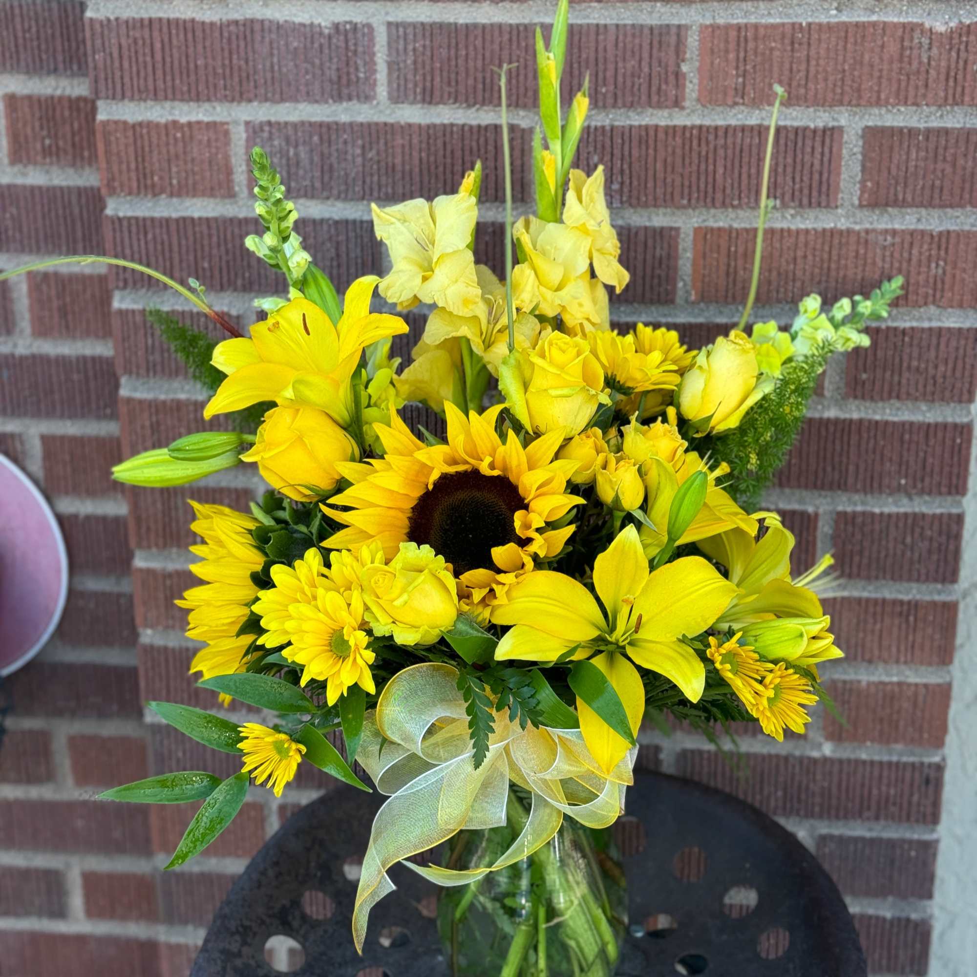 Yellow mixed flower bouquet in a glass vase with a ribbon