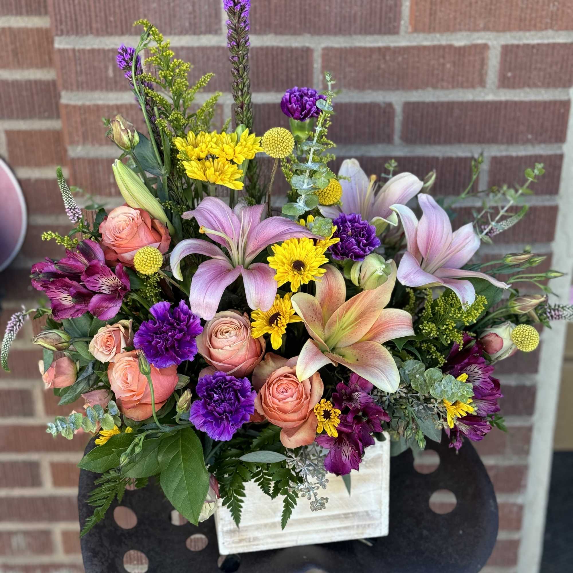 Mixed bouquet with pink lilies, roses, and purple flowers in a white container