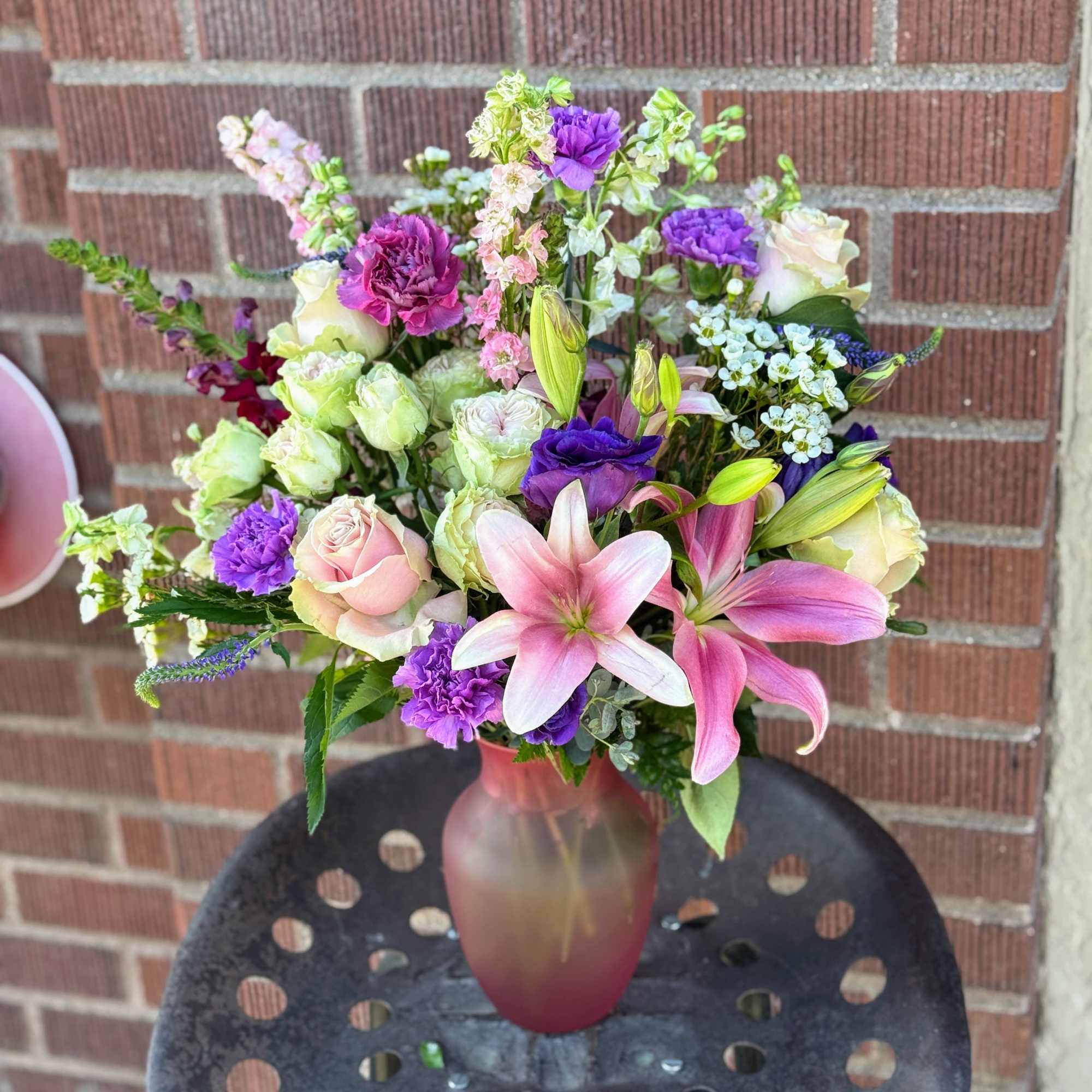 Mixed bouquet of pink lilies, roses, and purple flowers in a frosted vase