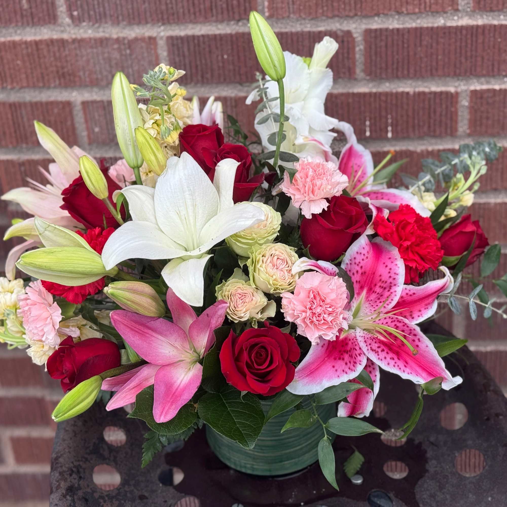 Mixed bouquet of red roses, lilies, and pink carnations in a green vase