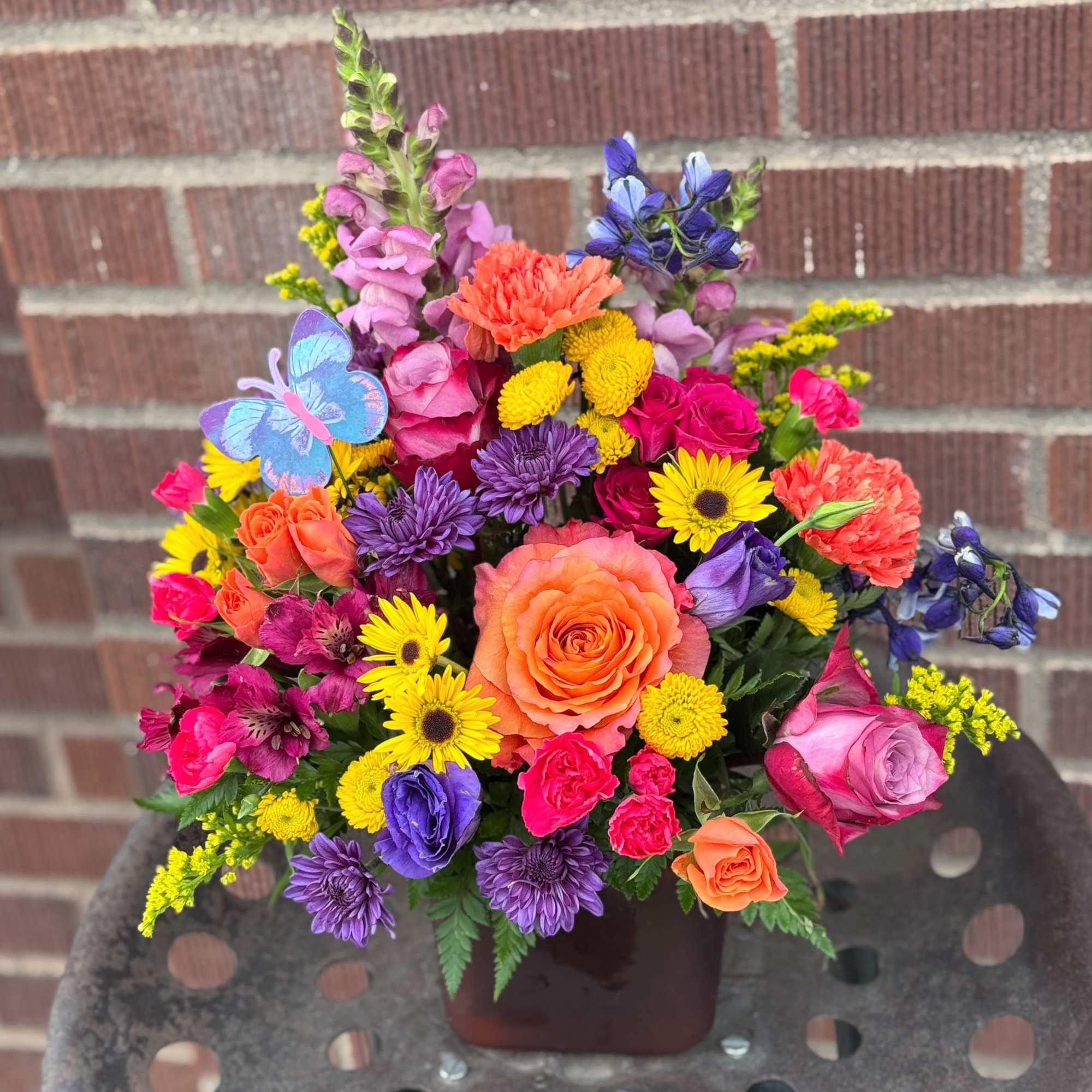 Colorful mixed bouquet in a square vase with roses, daisies, and snapdragons
