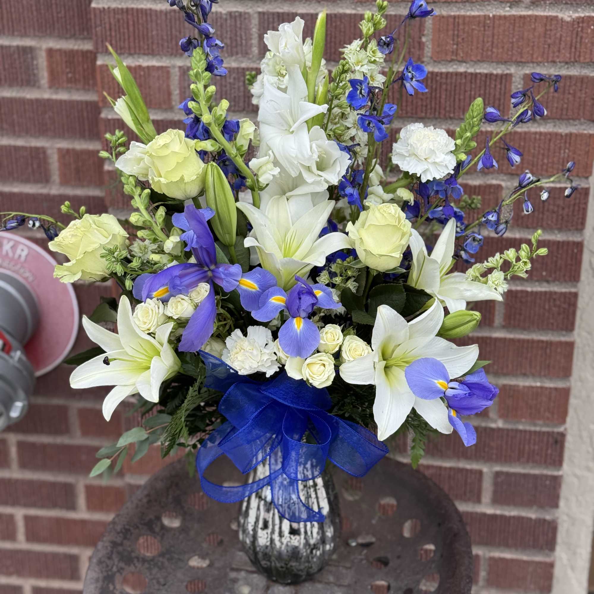 Bouquet of white lilies and blue flowers in a glass vase with a blue ribbon