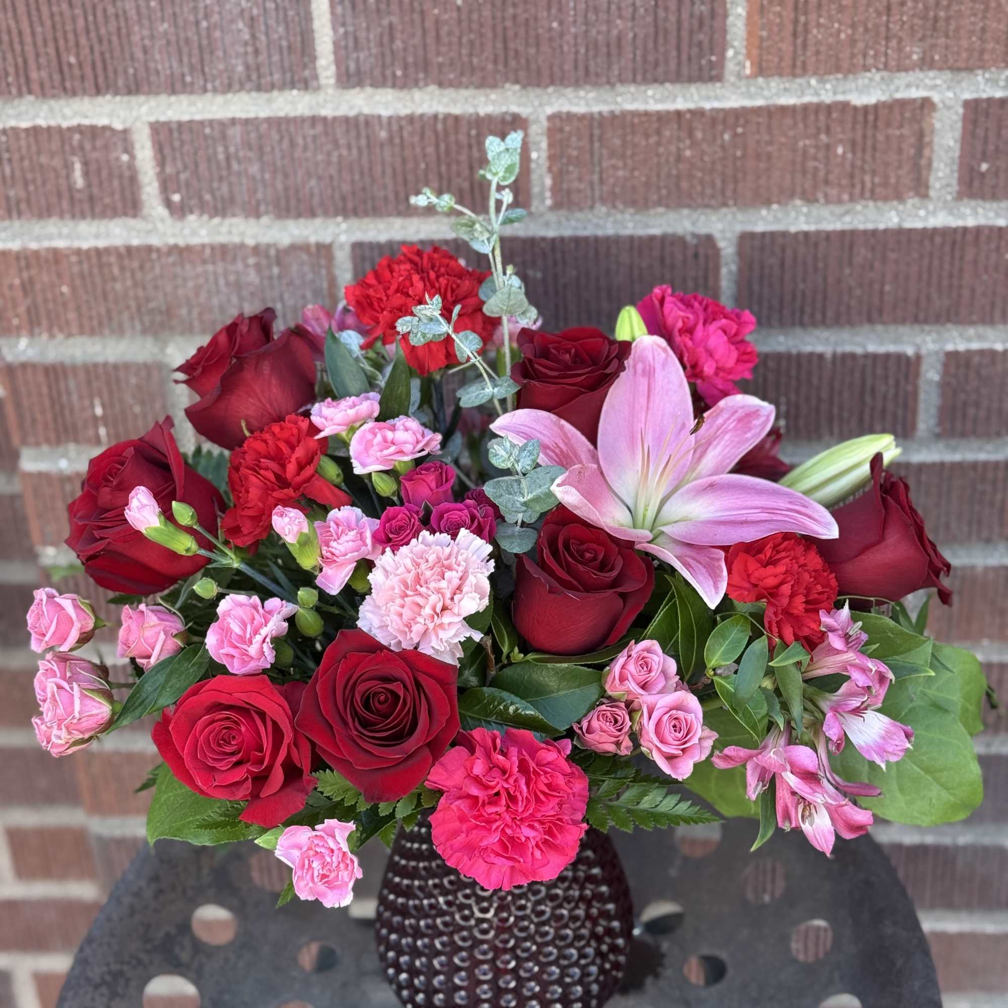 Bouquet of red and pink roses with lilies in a dark vase