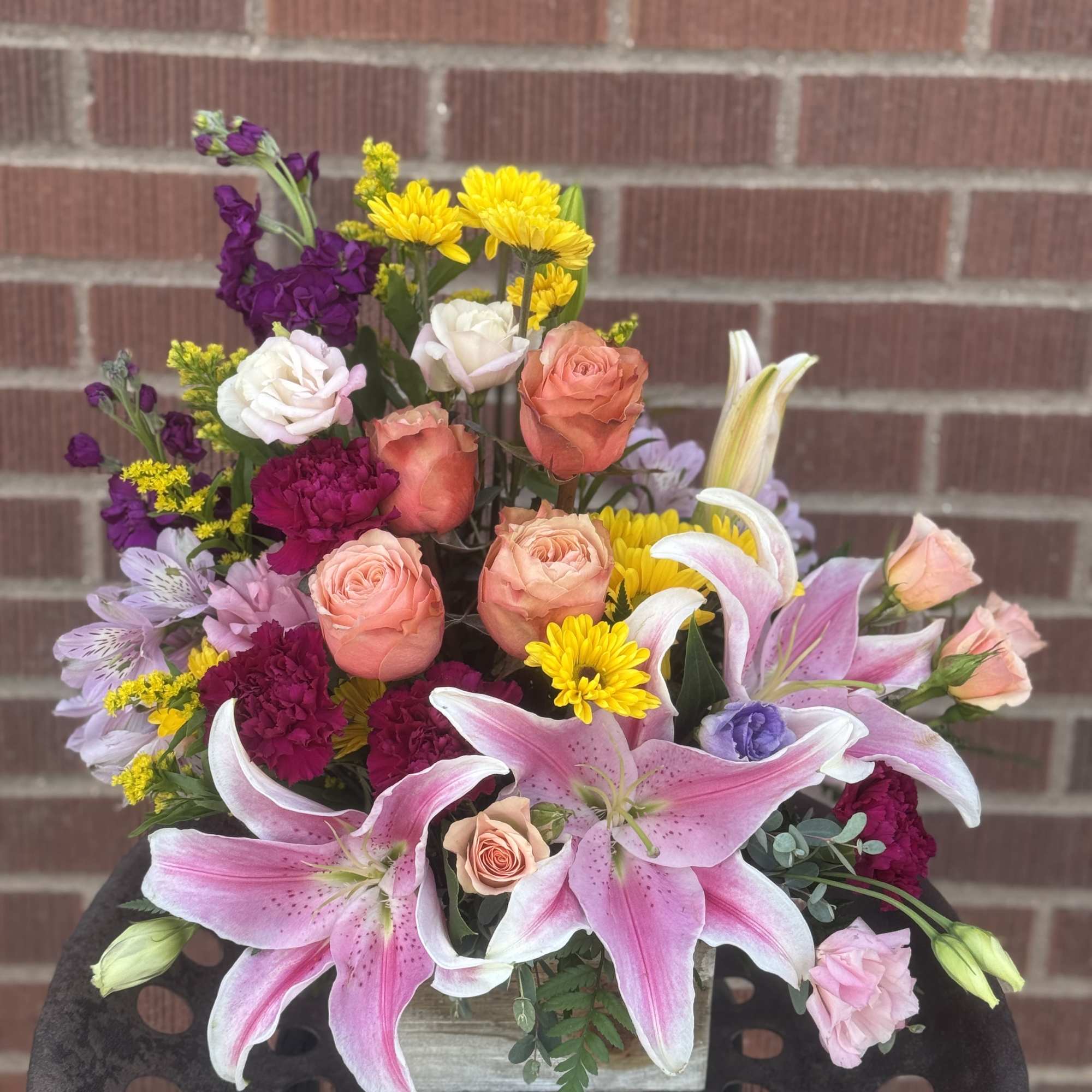 Mixed bouquet with pink lilies, roses, and yellow daisies in a wooden container