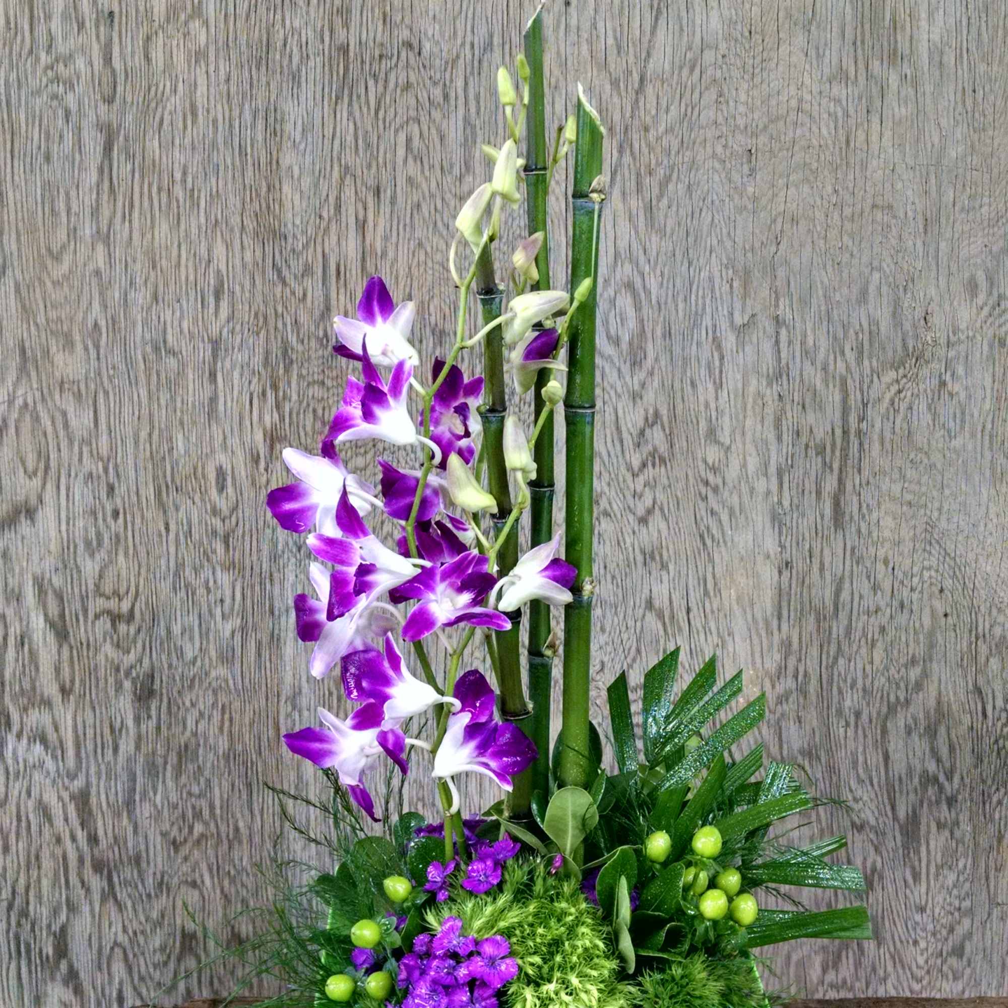 Purple and white orchids in a lime green vase with a small glass candle holder