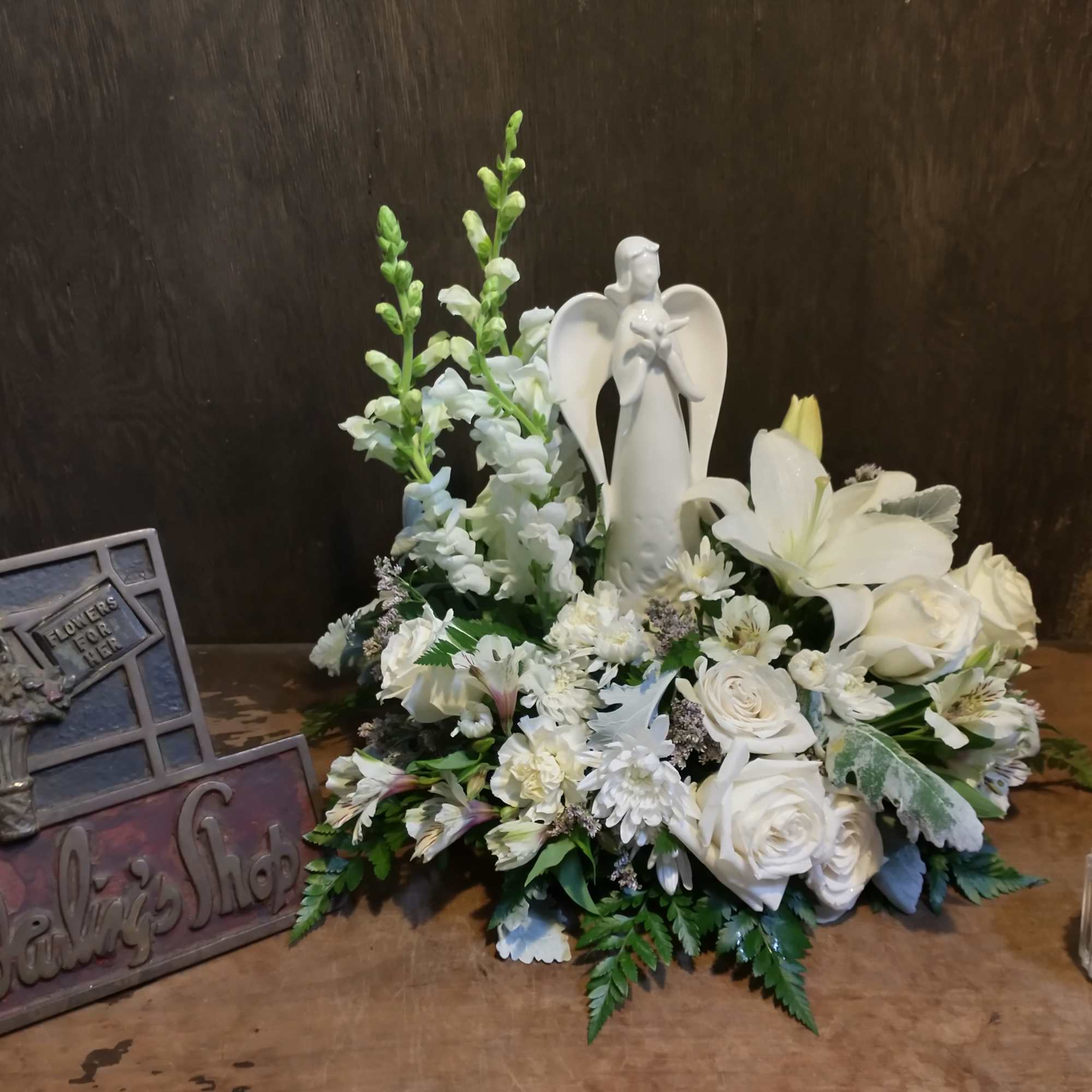 White floral arrangement with an angel figurine and roses on a table