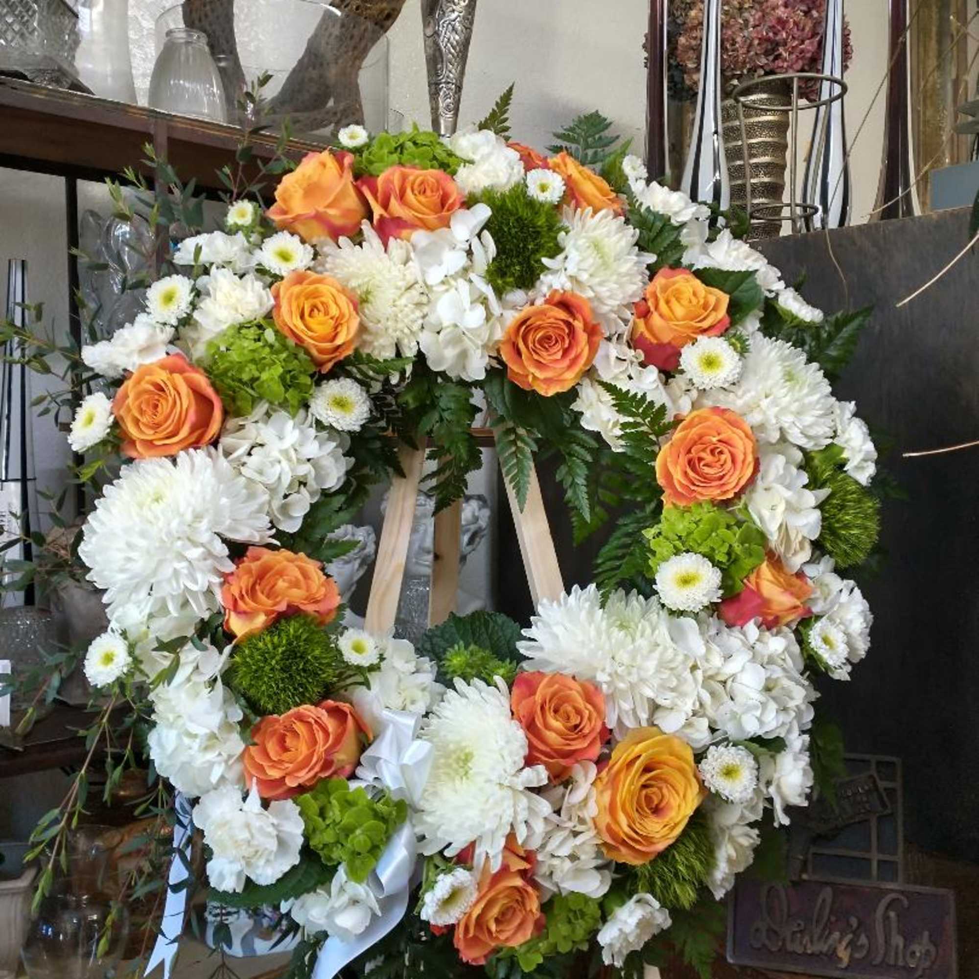 Circular floral wreath with orange roses and white blooms on a stand