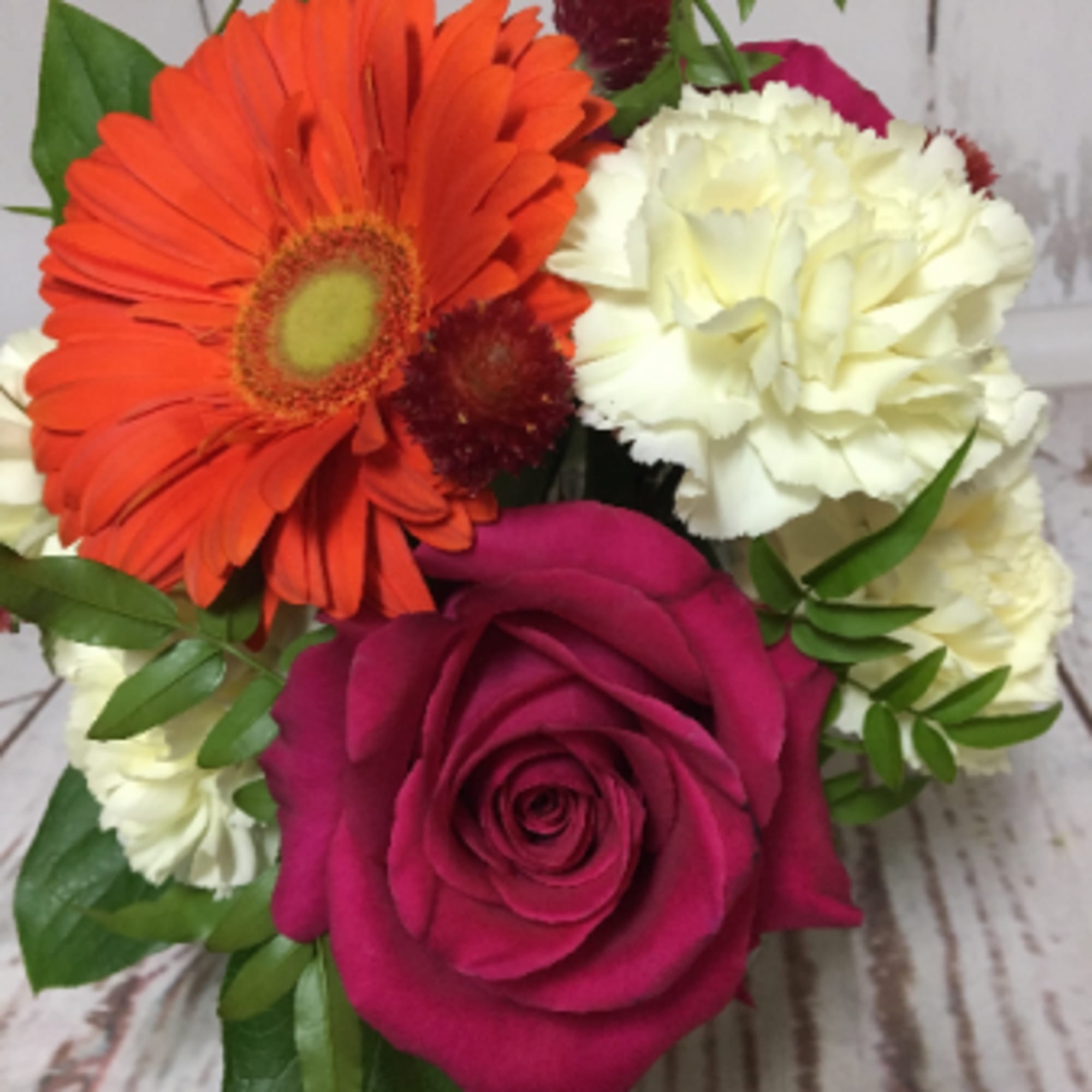 Compact arrangement with orange gerbera, pink rose, white carnations, and red accent blooms.