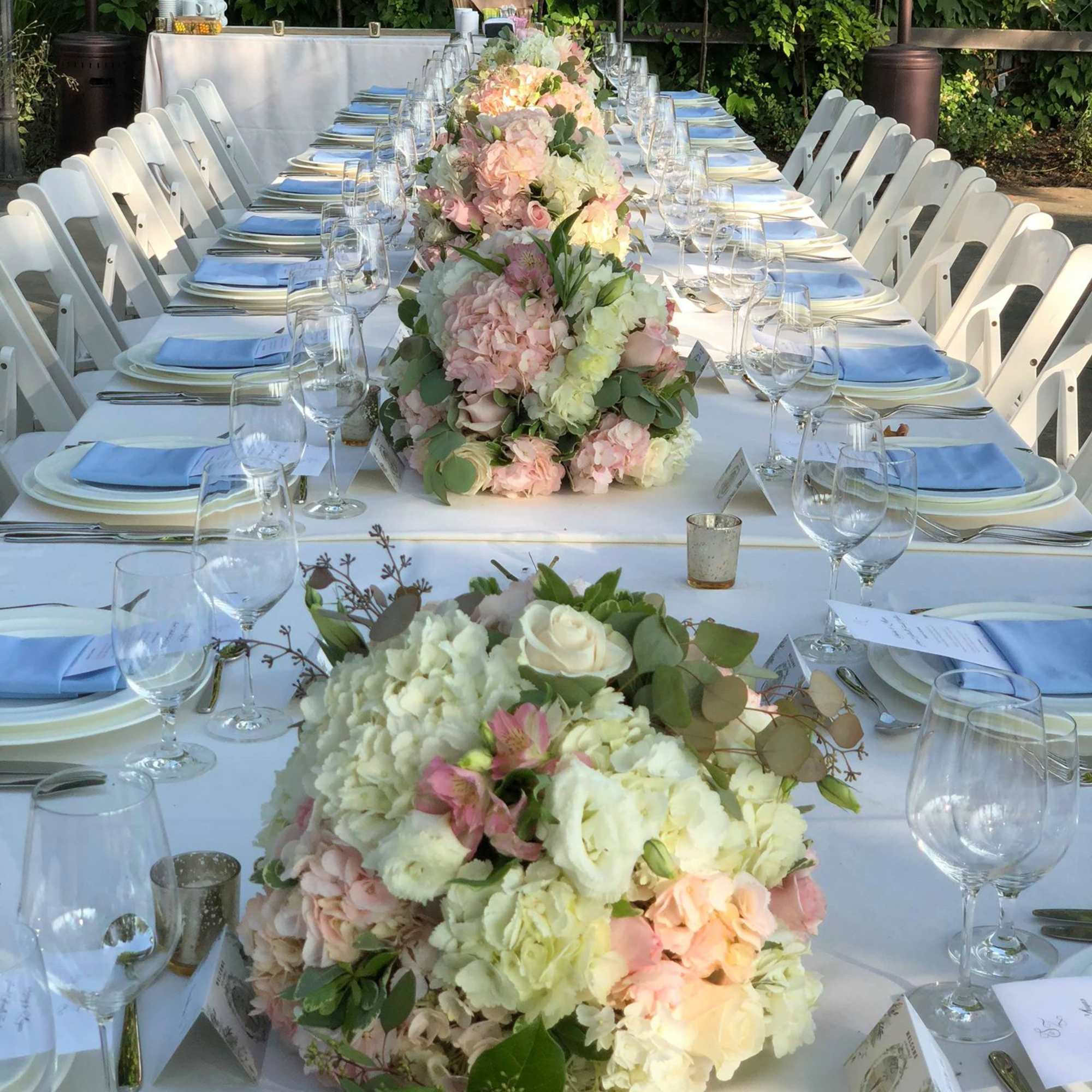 Long banquet table with pastel floral centerpieces and blue napkins