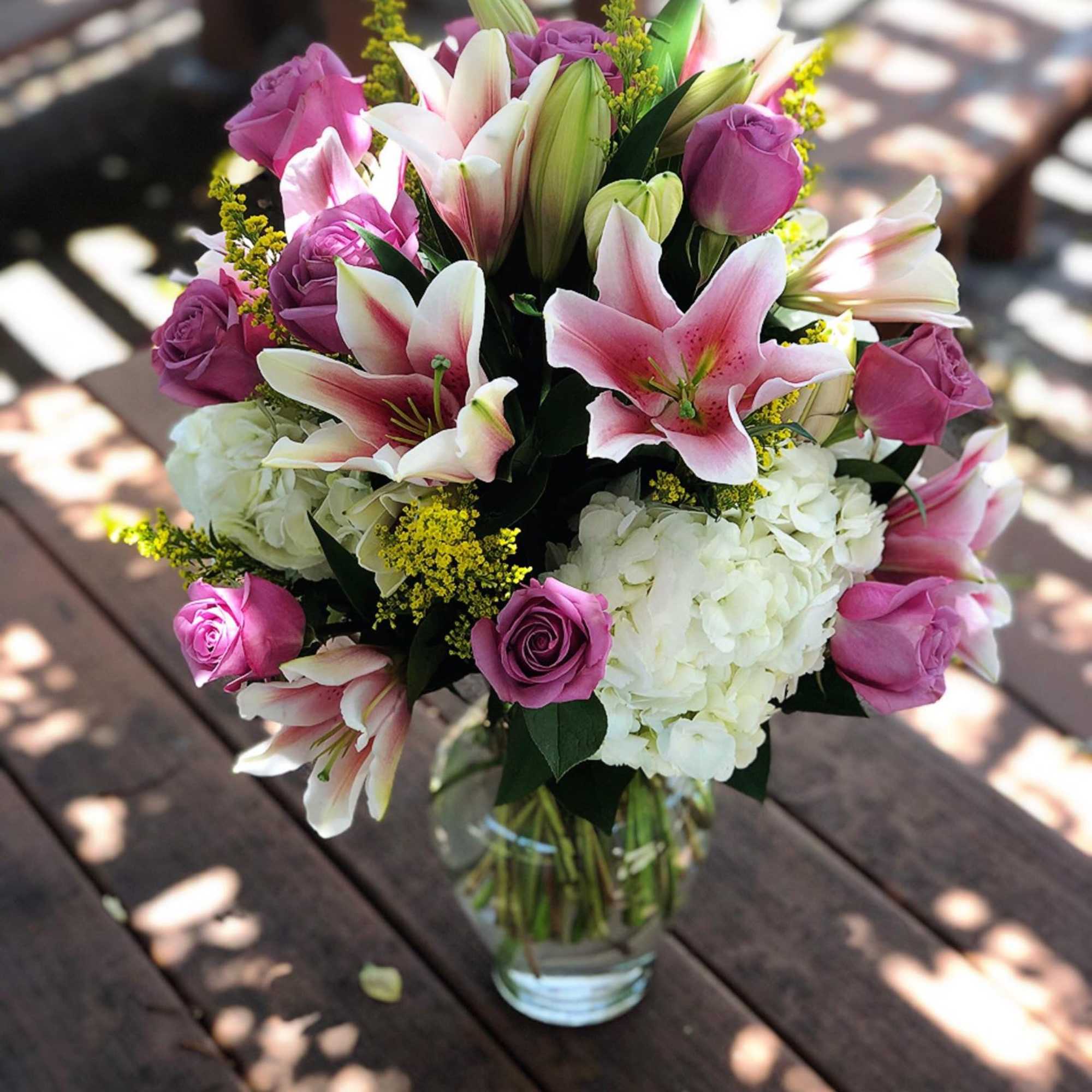 Pink roses and lilies arranged in a glass vase with white hydrangeas