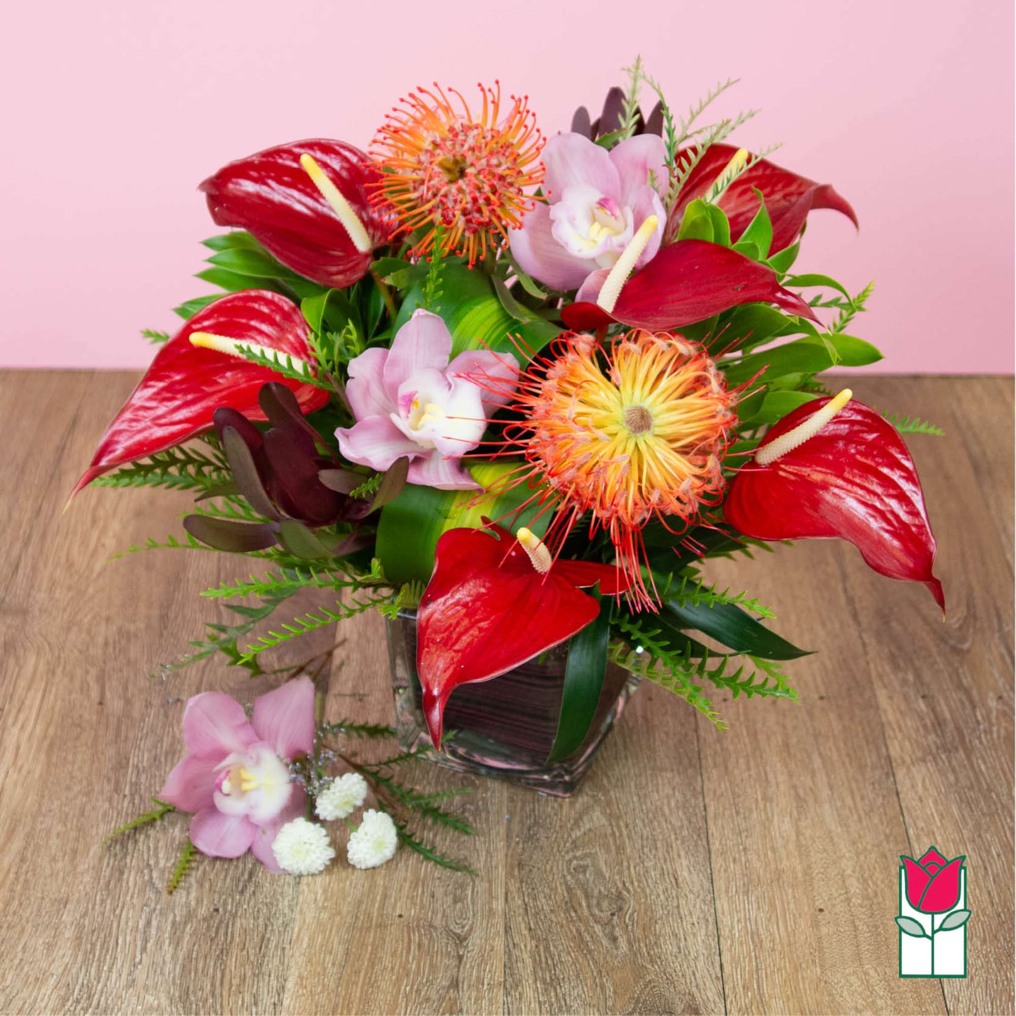 Tropical floral arrangement in a clear square vase with red anthuriums and pink orchids