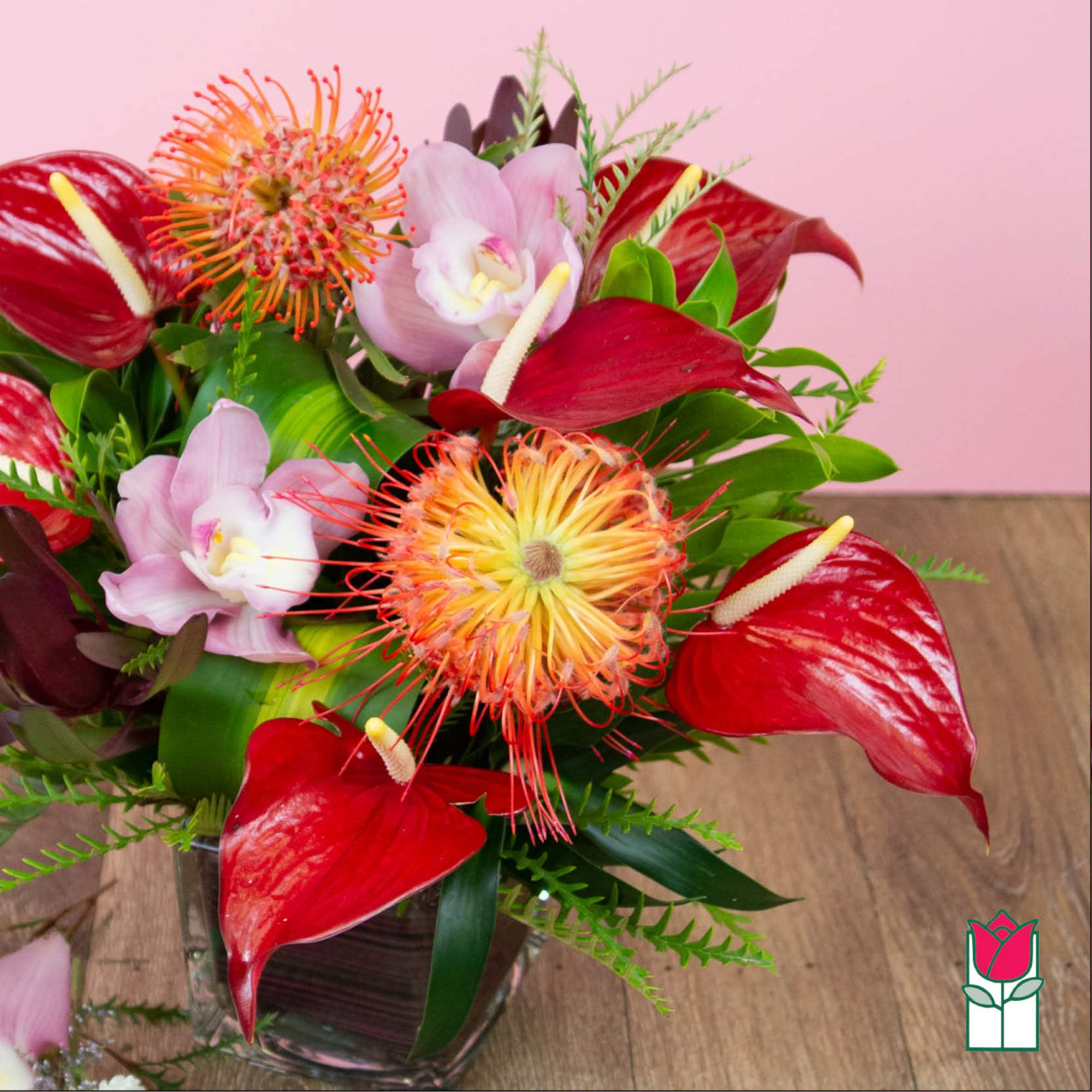 Tropical bouquet with red anthuriums and pink orchids in a glass vase