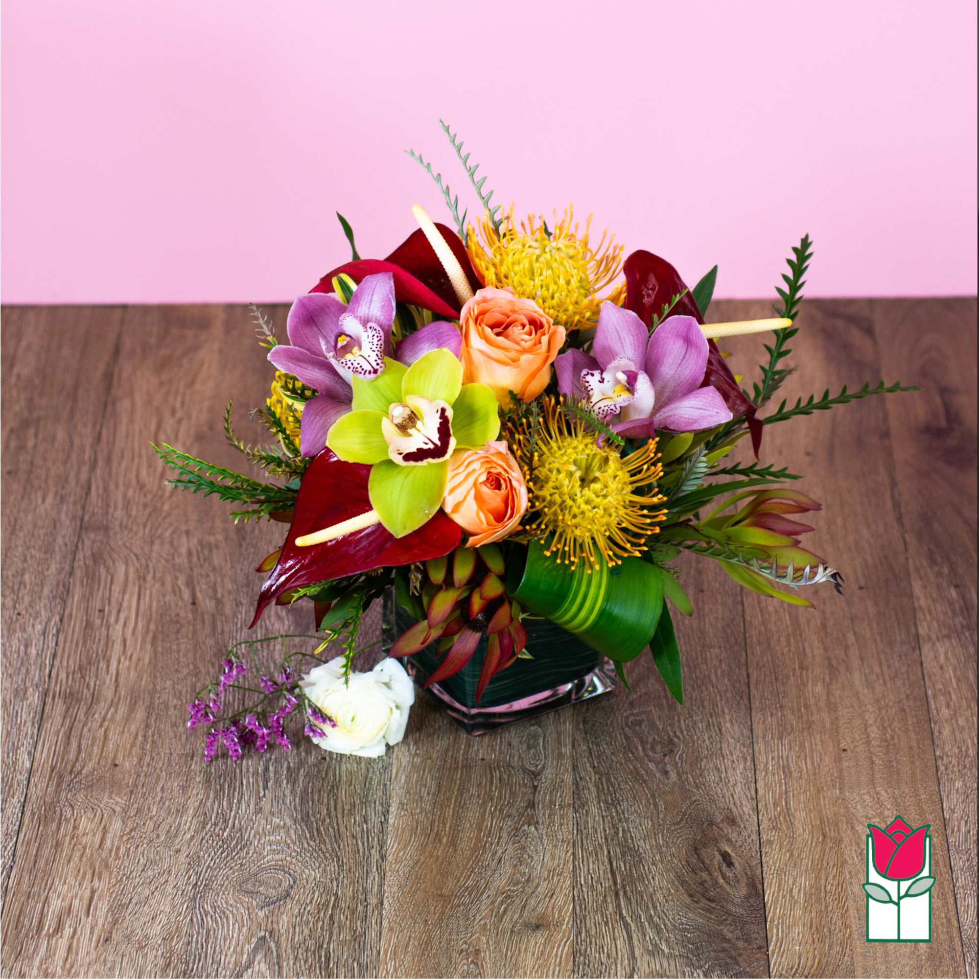 Tropical bouquet with orchids, roses, and yellow pincushion blooms in a glass vase