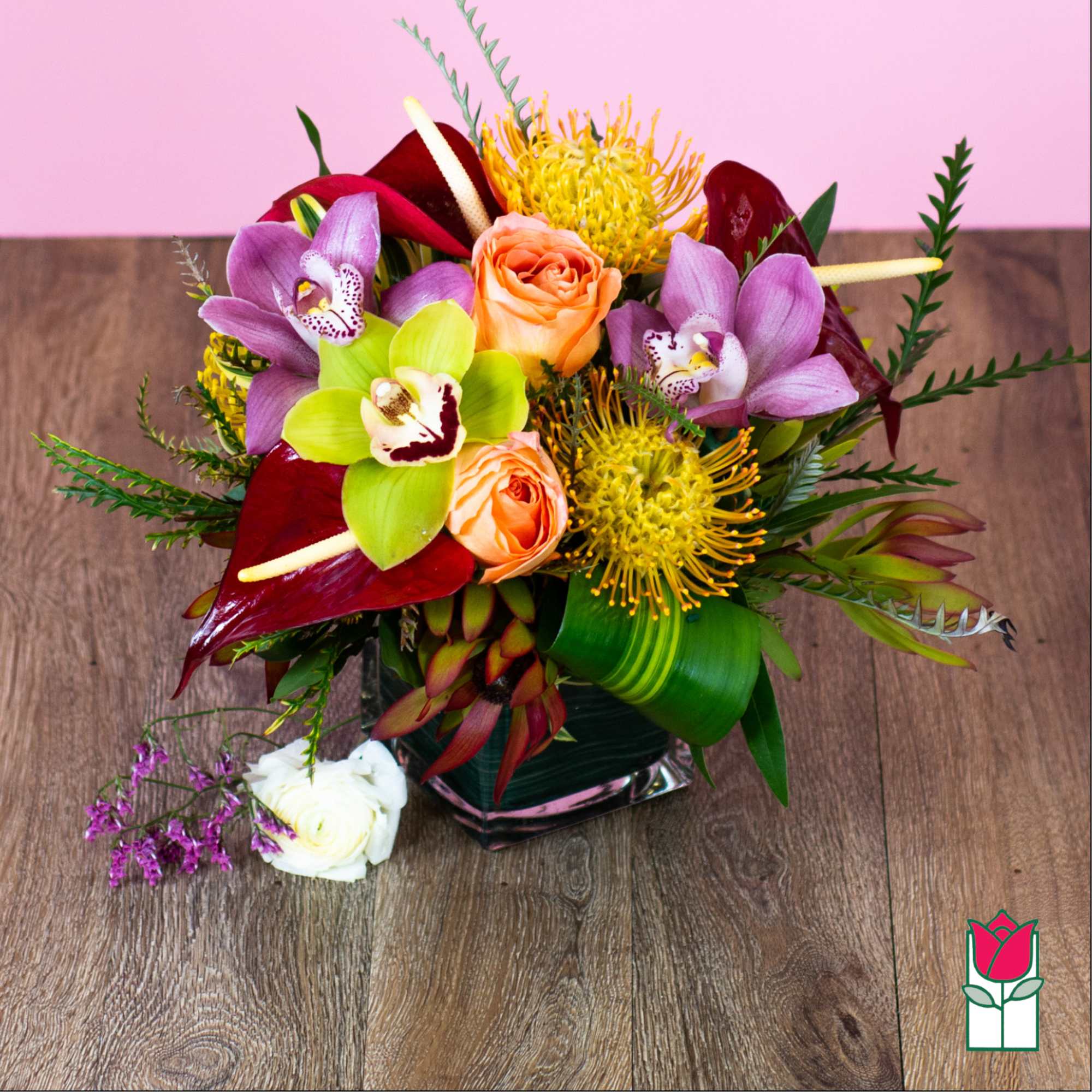 Mixed tropical bouquet in a square glass vase with orchids and roses