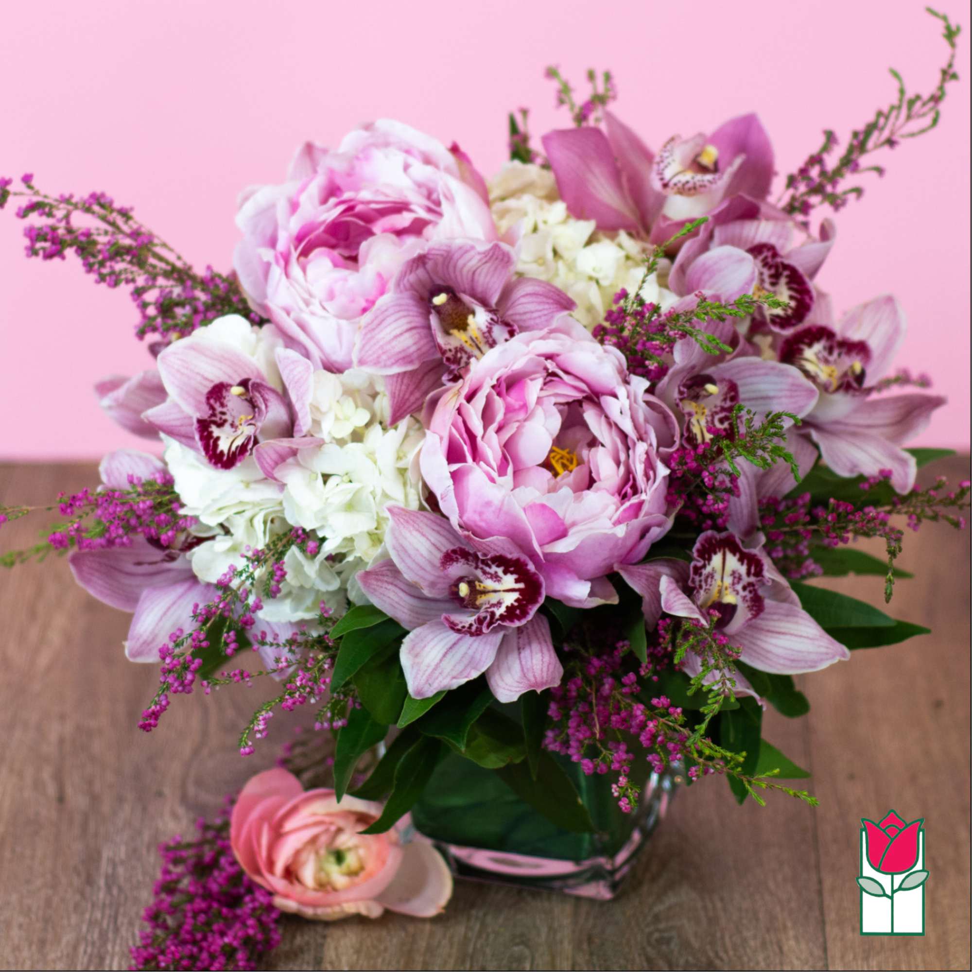 Pink peonies and orchids in a glass vase with purple filler flowers