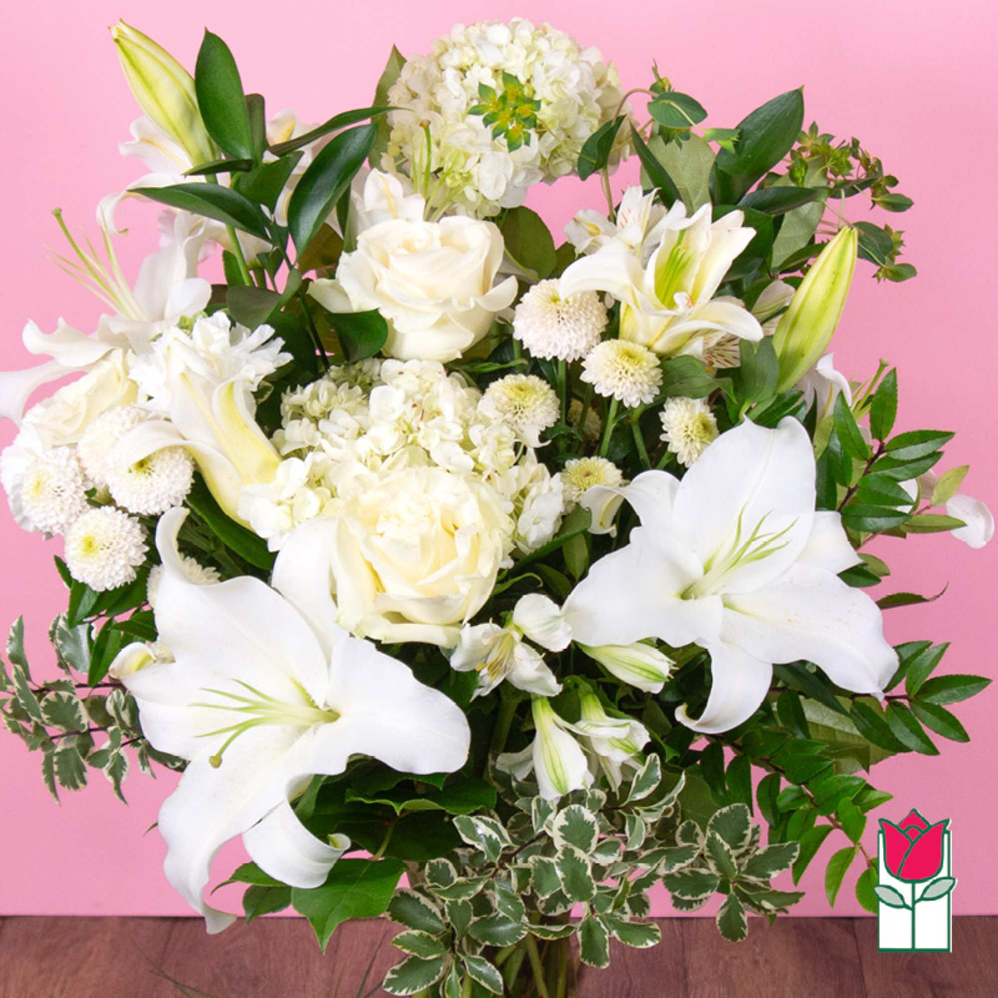 White lilies and roses arranged with green foliage against a pink background