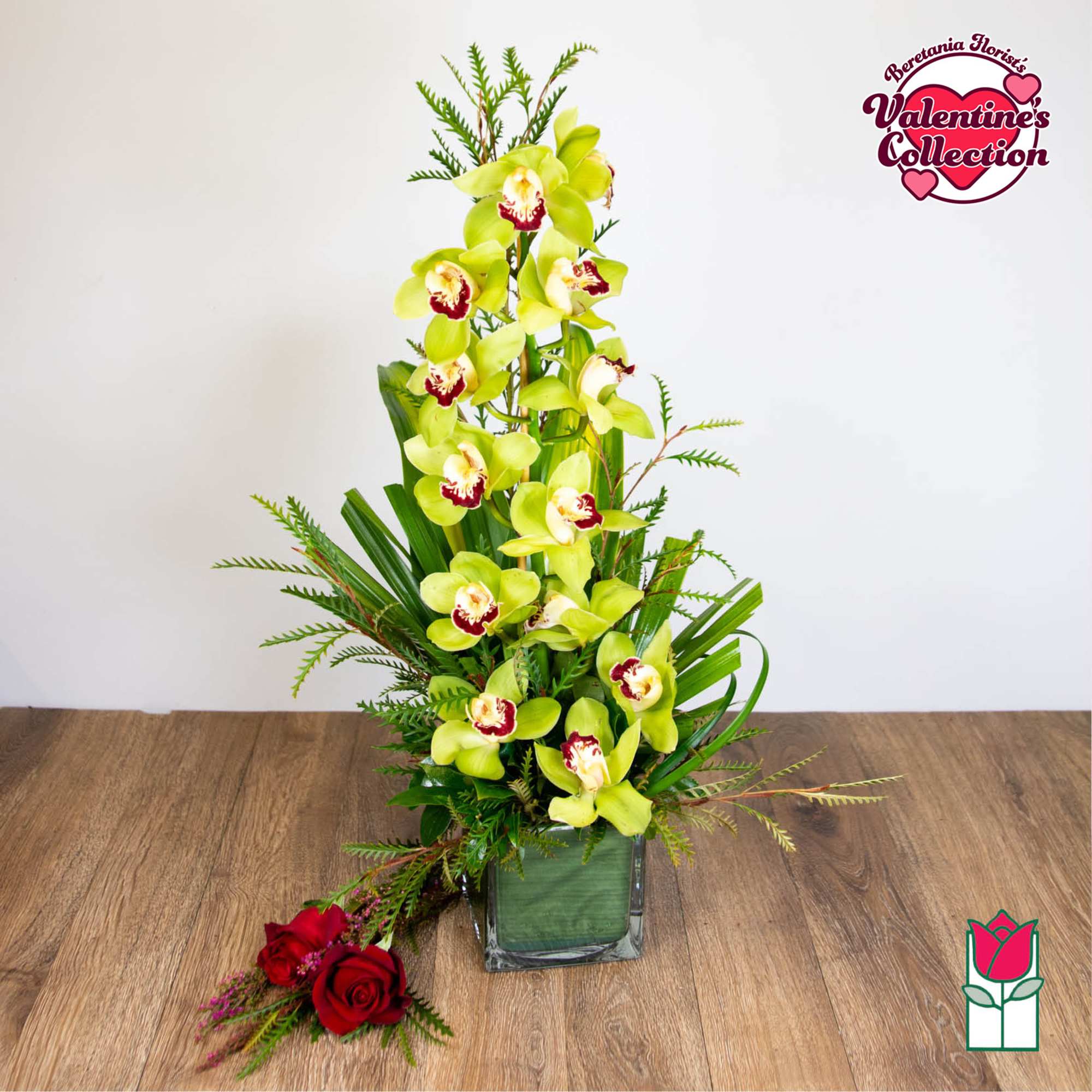 Tall yellow-green cymbidium orchid arrangement with red accents in a square glass vase