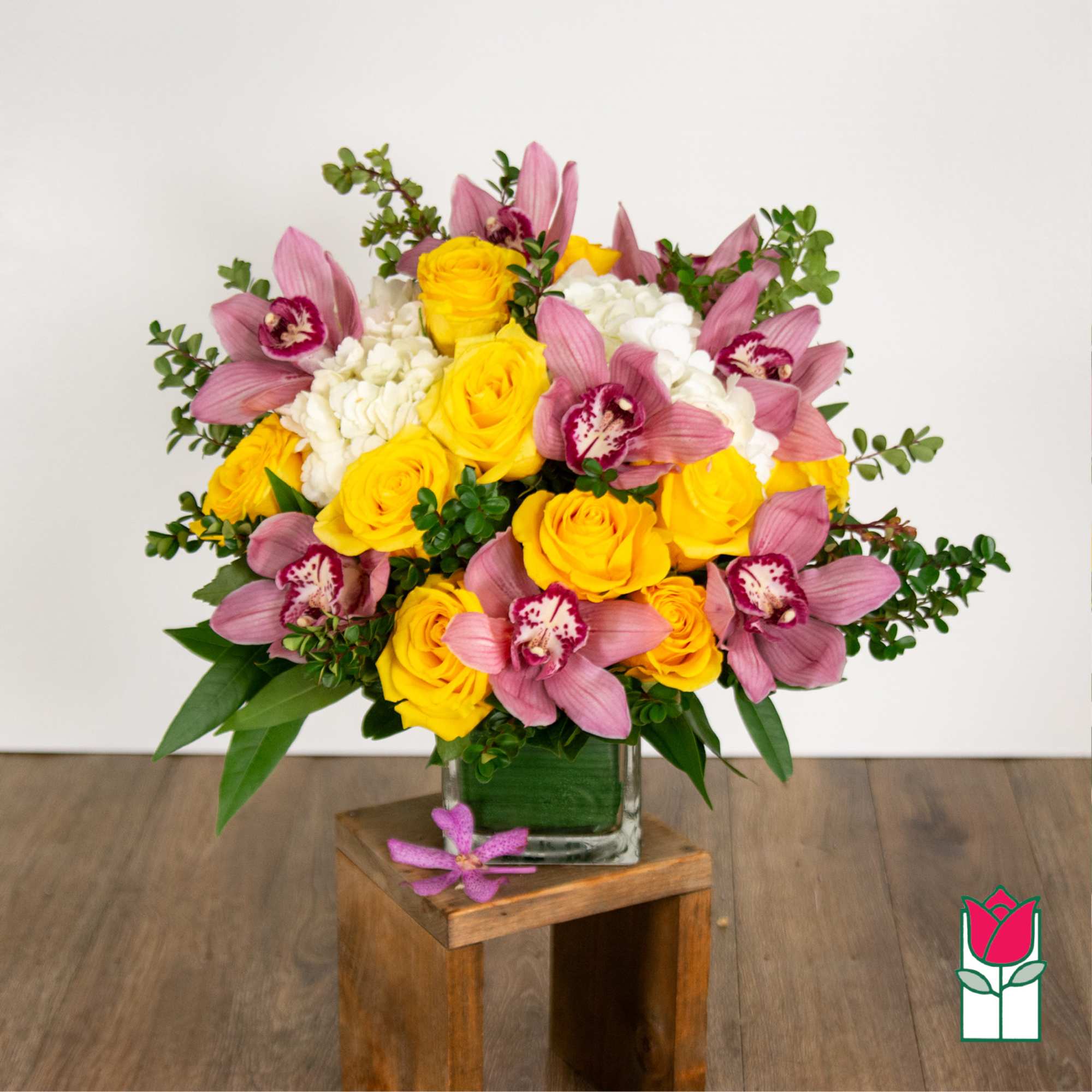 Yellow roses and pink orchids arranged in a glass vase