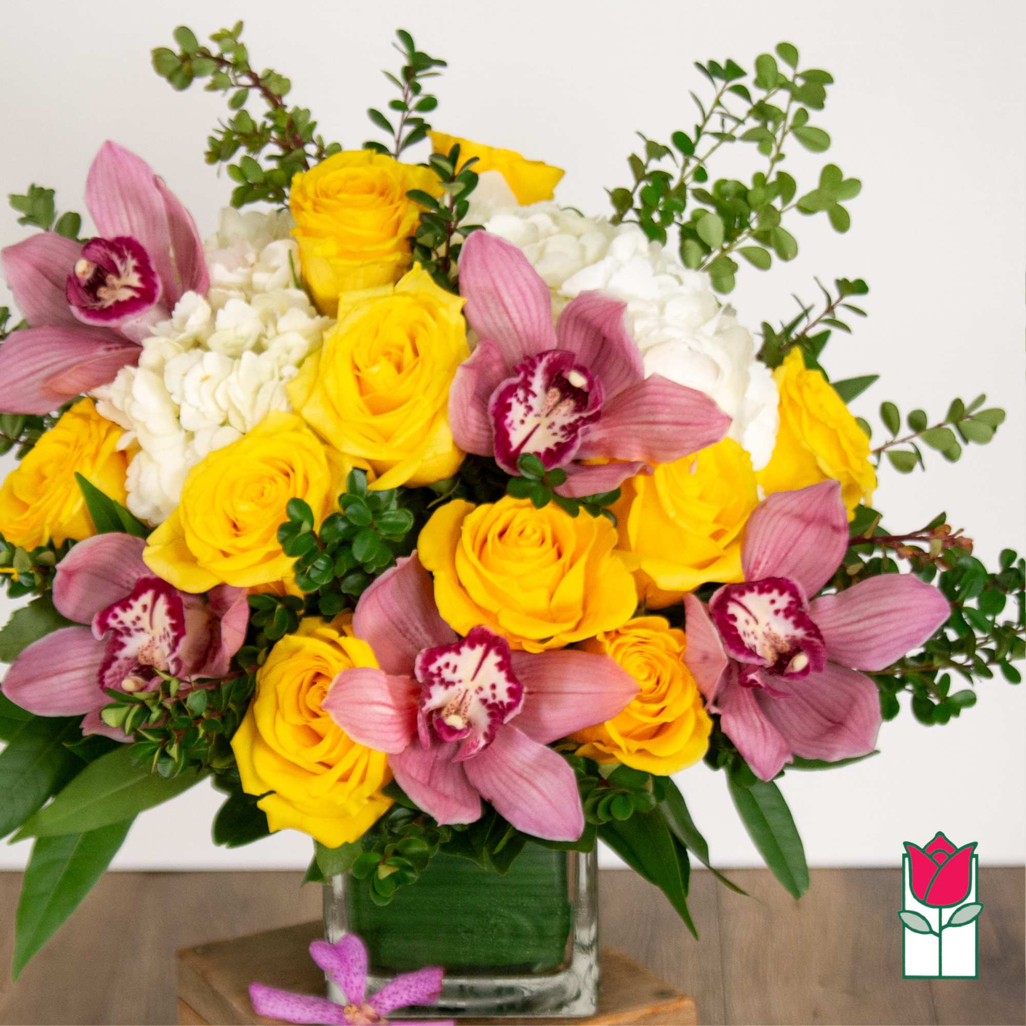 Yellow roses and pink orchids in a clear glass vase