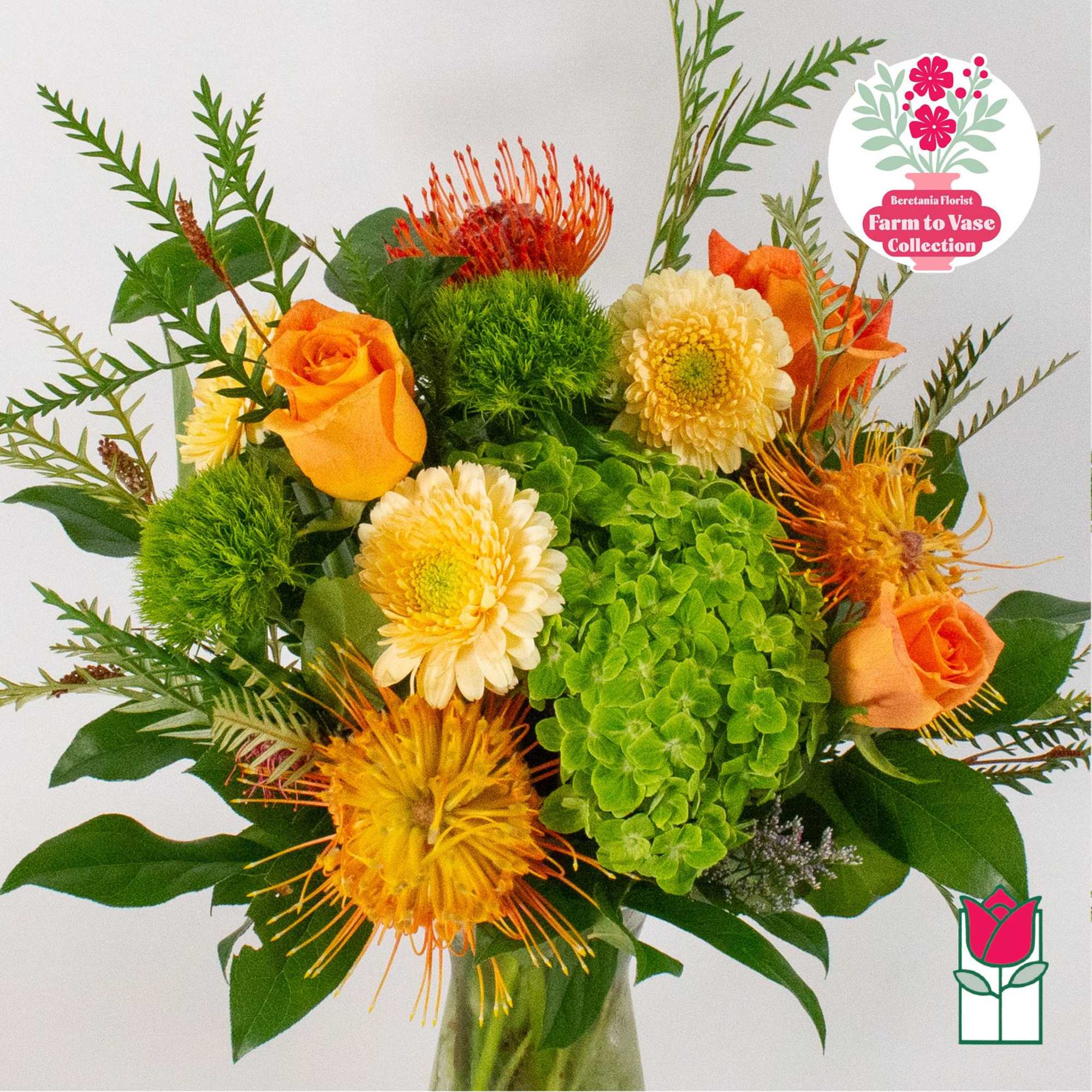 Bouquet of orange roses, green hydrangea, and yellow spider mums in a glass vase