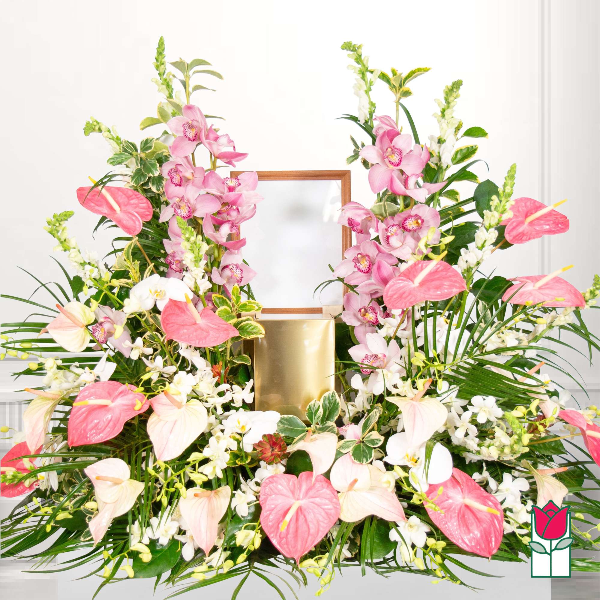 Pink orchids and anthuriums arranged around a gold urn and wooden frame