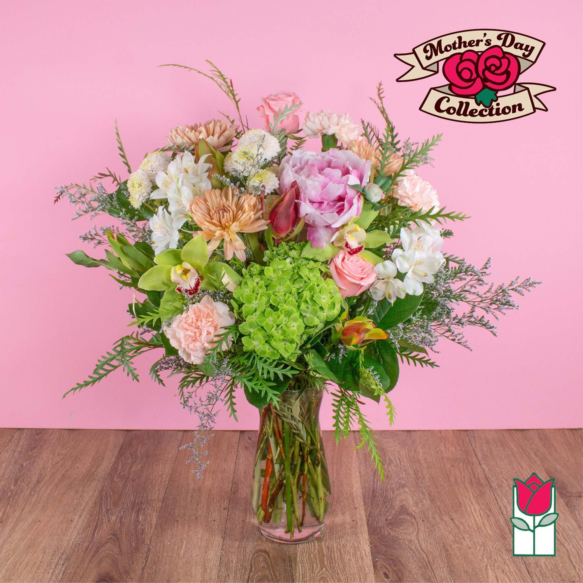 Tall mixed bouquet of pink, white, peach, and green flowers in a clear glass vase against a pink background.