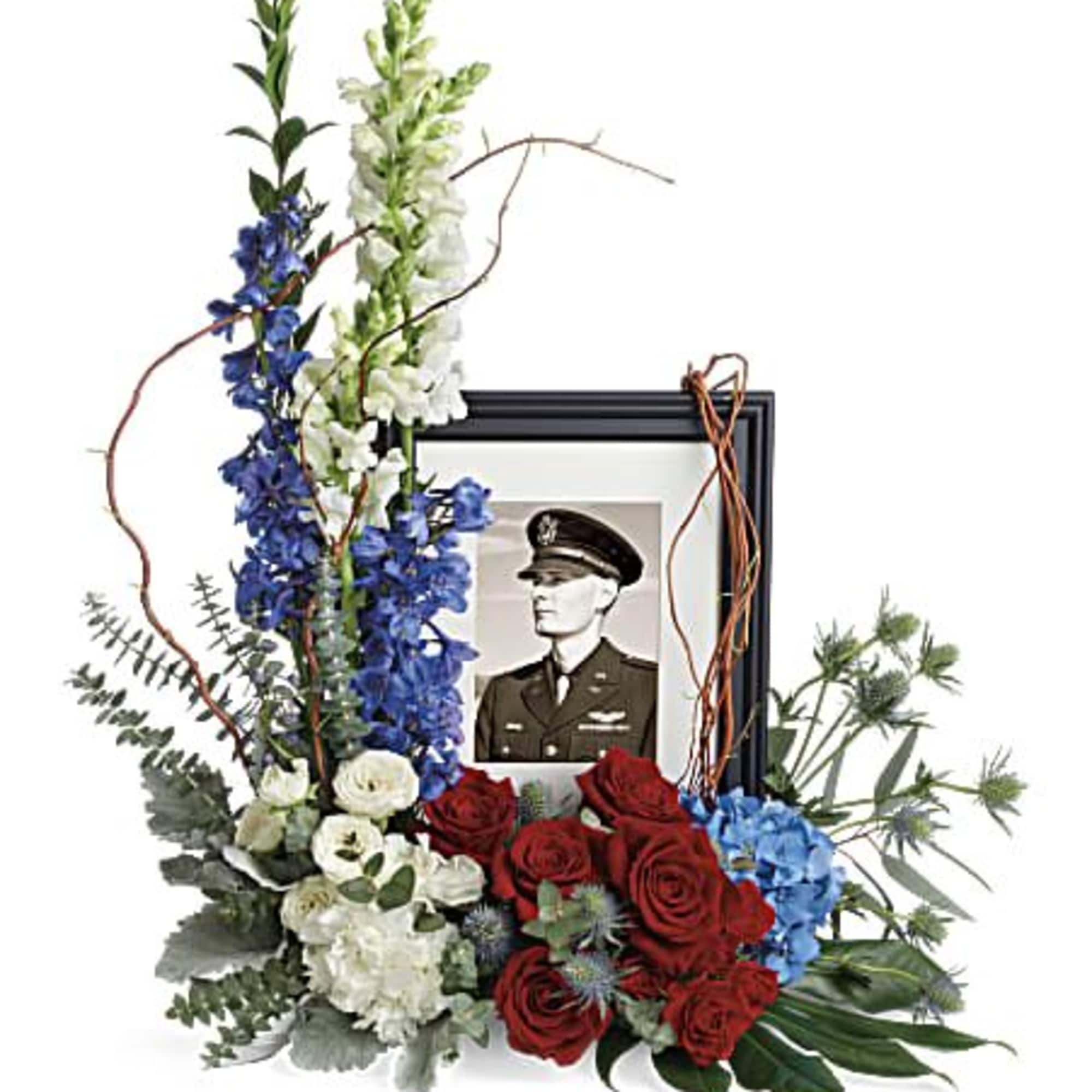 Red, white, and blue floral tribute arranged around a black picture frame with a military portrait.