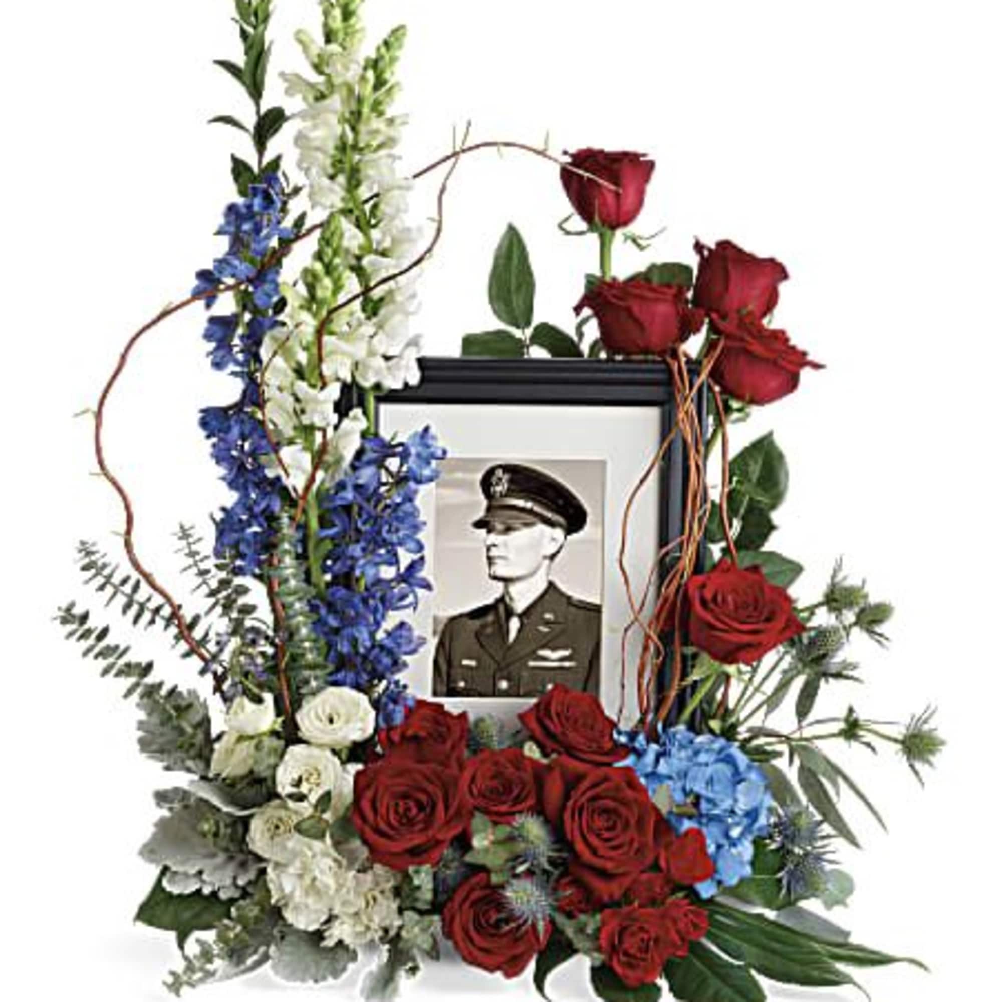 Tall red, white, and blue memorial floral arrangement surrounding a black picture frame with a portrait.