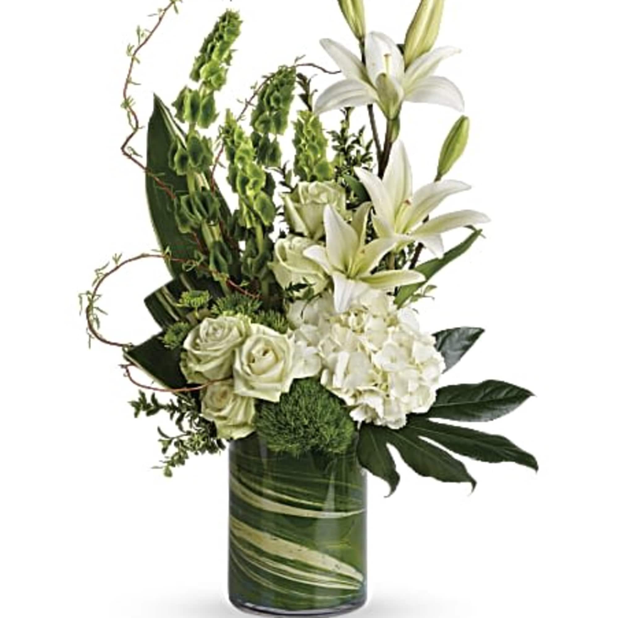 Tall white lilies, roses, and hydrangeas with green accents arranged in a clear glass cylinder vase.