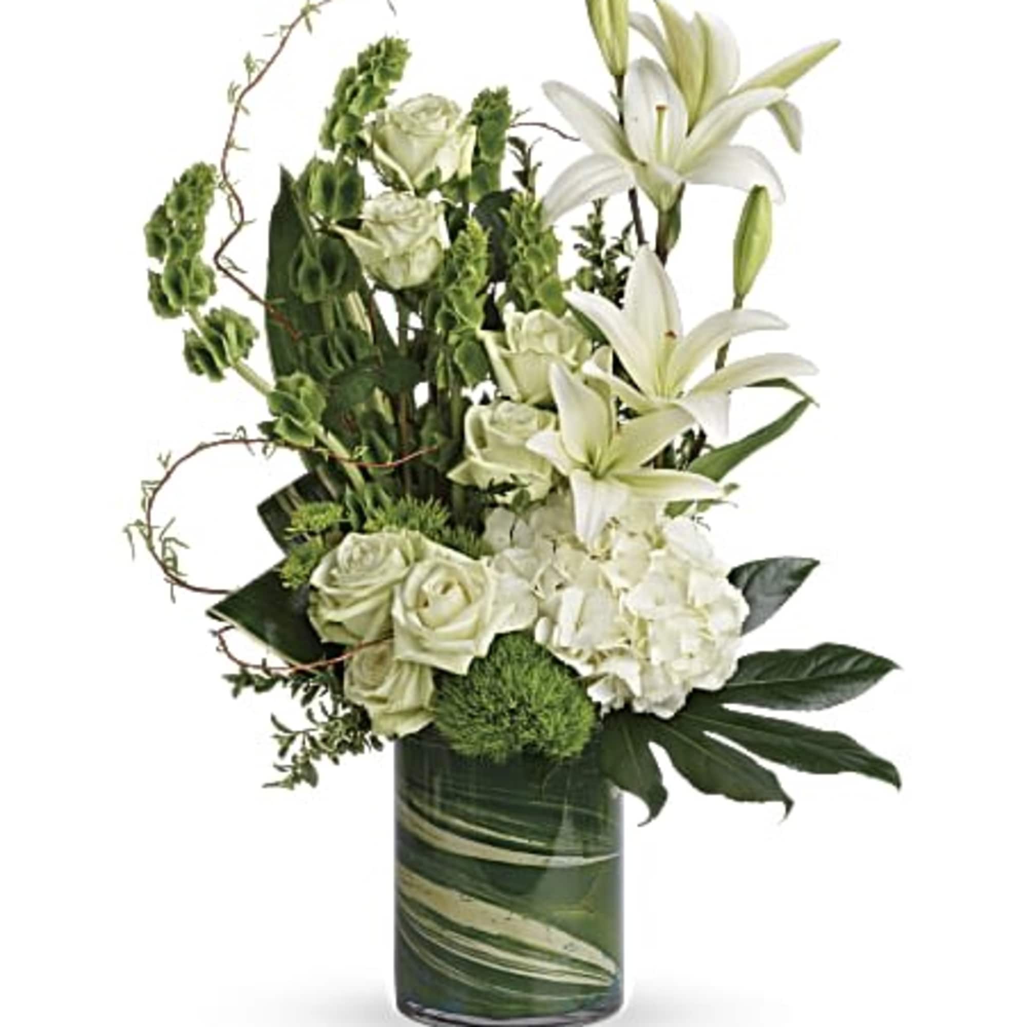 Tall white and green arrangement with lilies, roses, and hydrangeas in a clear cylinder vase lined with green leaves