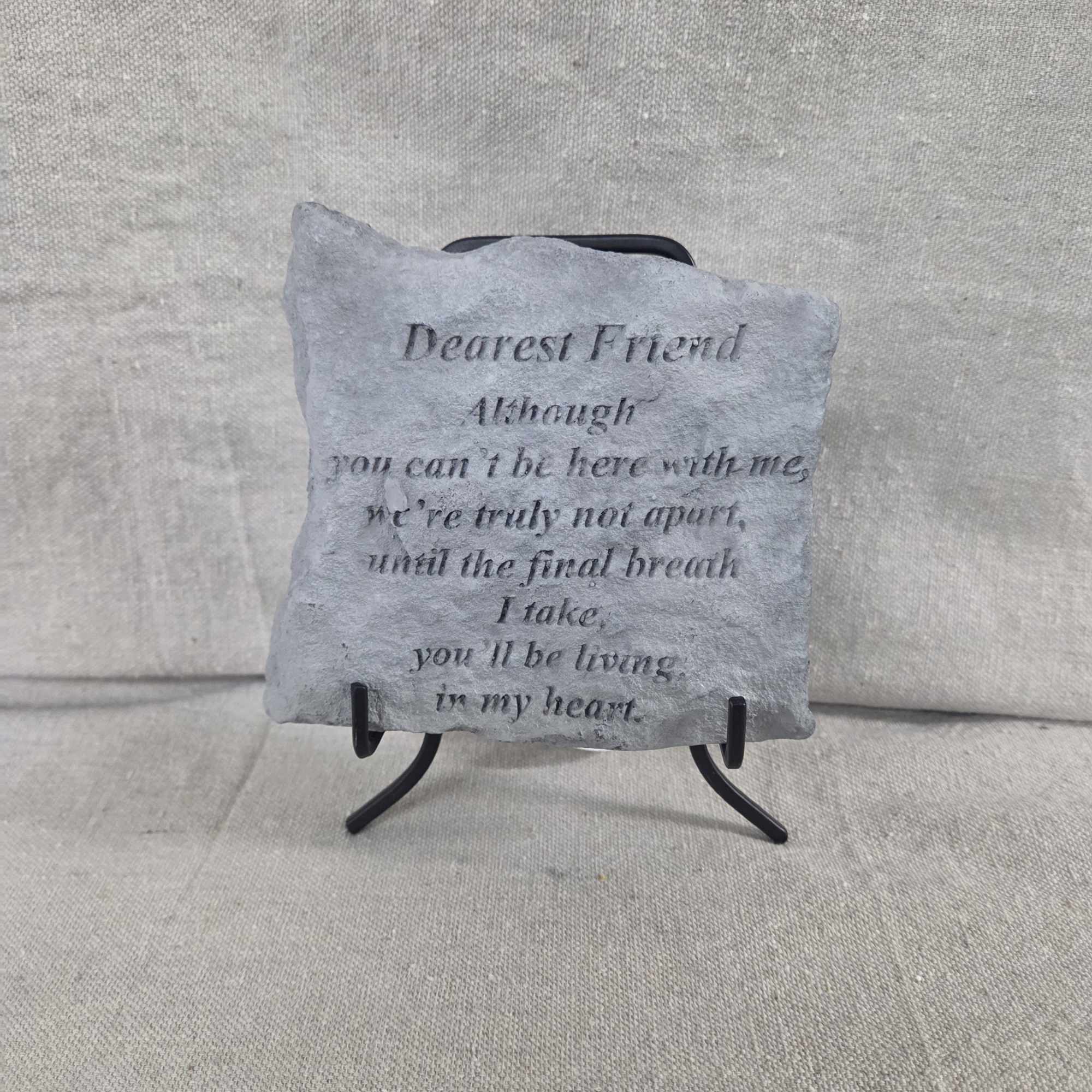 Small gray memorial stone plaque with engraved poem on a black metal stand against a neutral fabric backdrop.