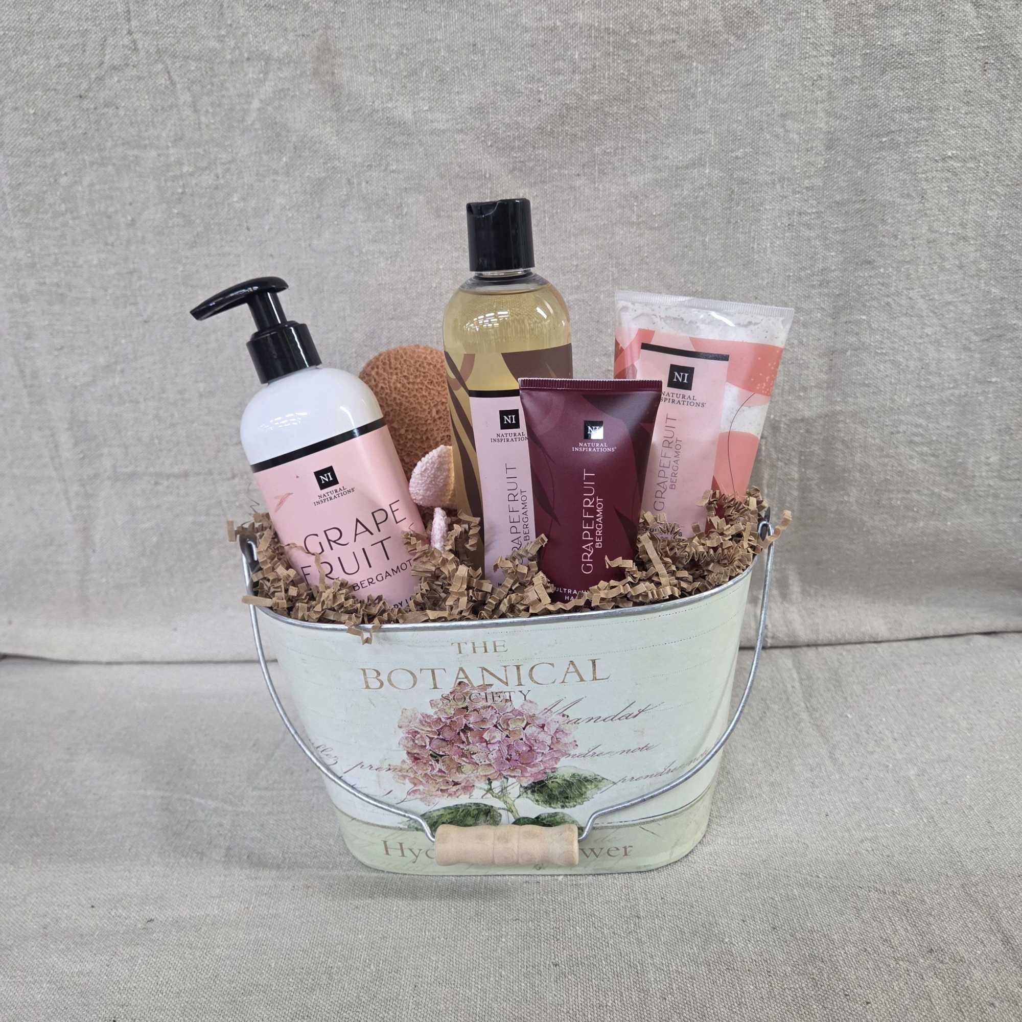 Grapefruit-scented bath gift set arranged in a floral metal pail with crinkle paper filler