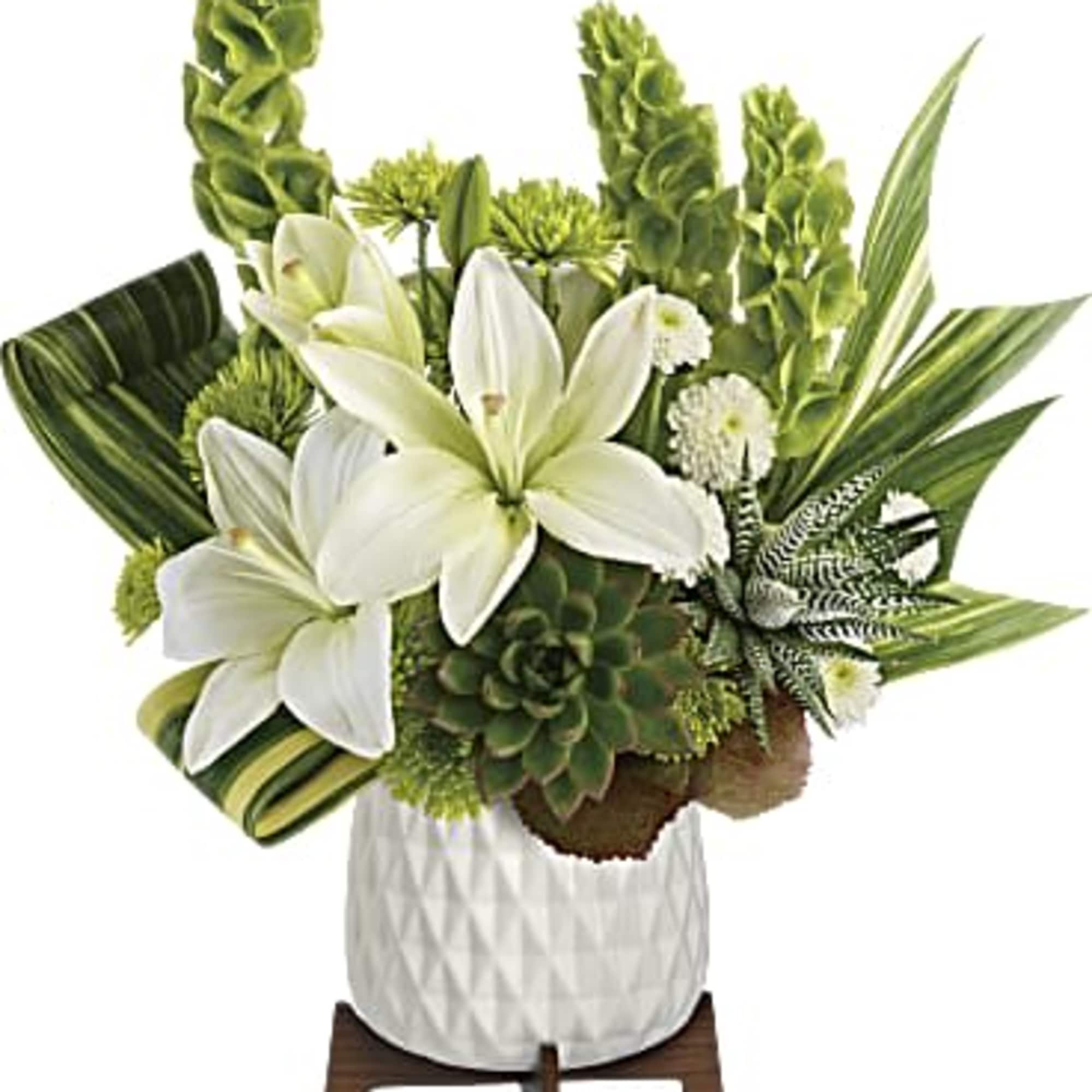 White lilies and green tropical foliage in a white vase