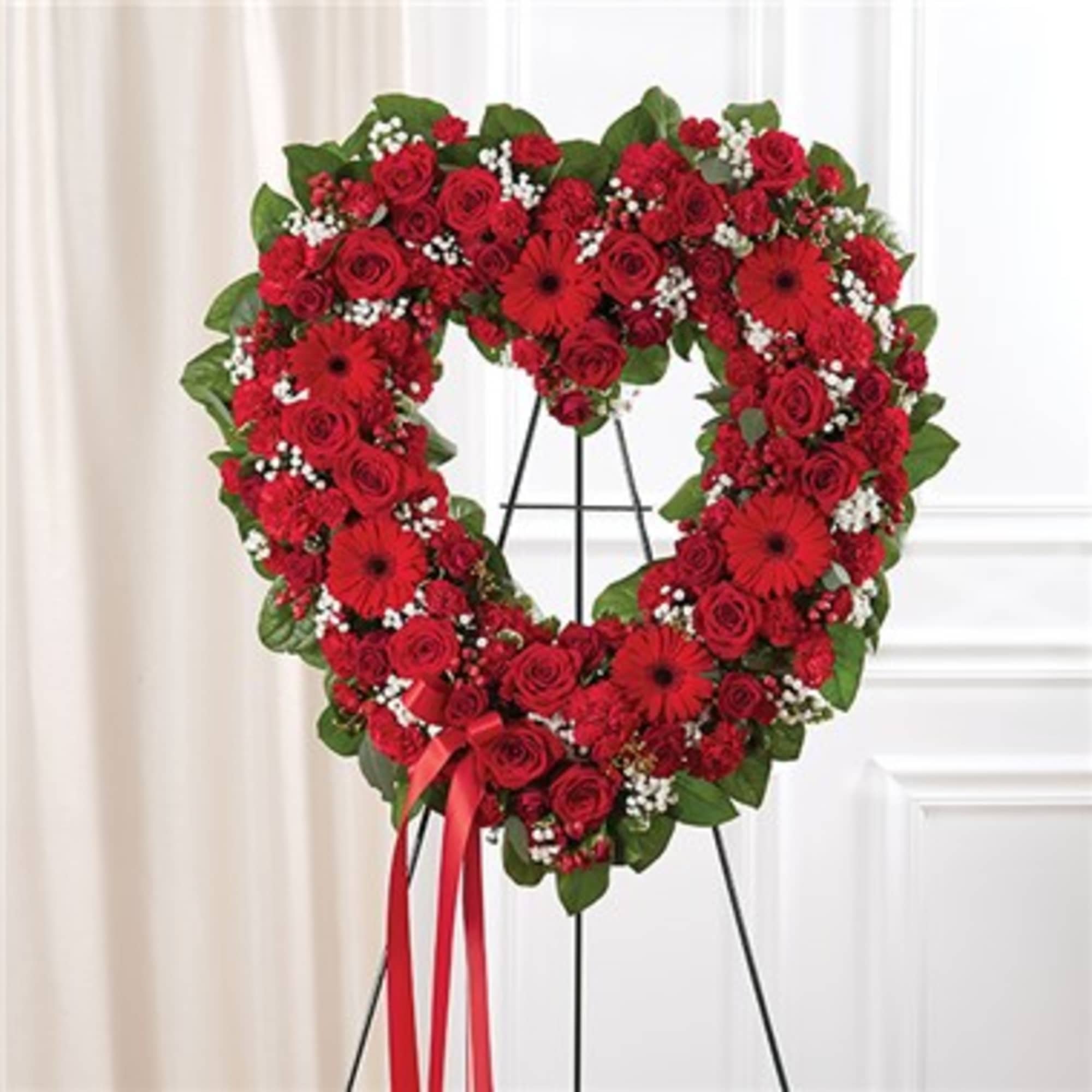 Heart-shaped red rose wreath on a black stand with a ribbon