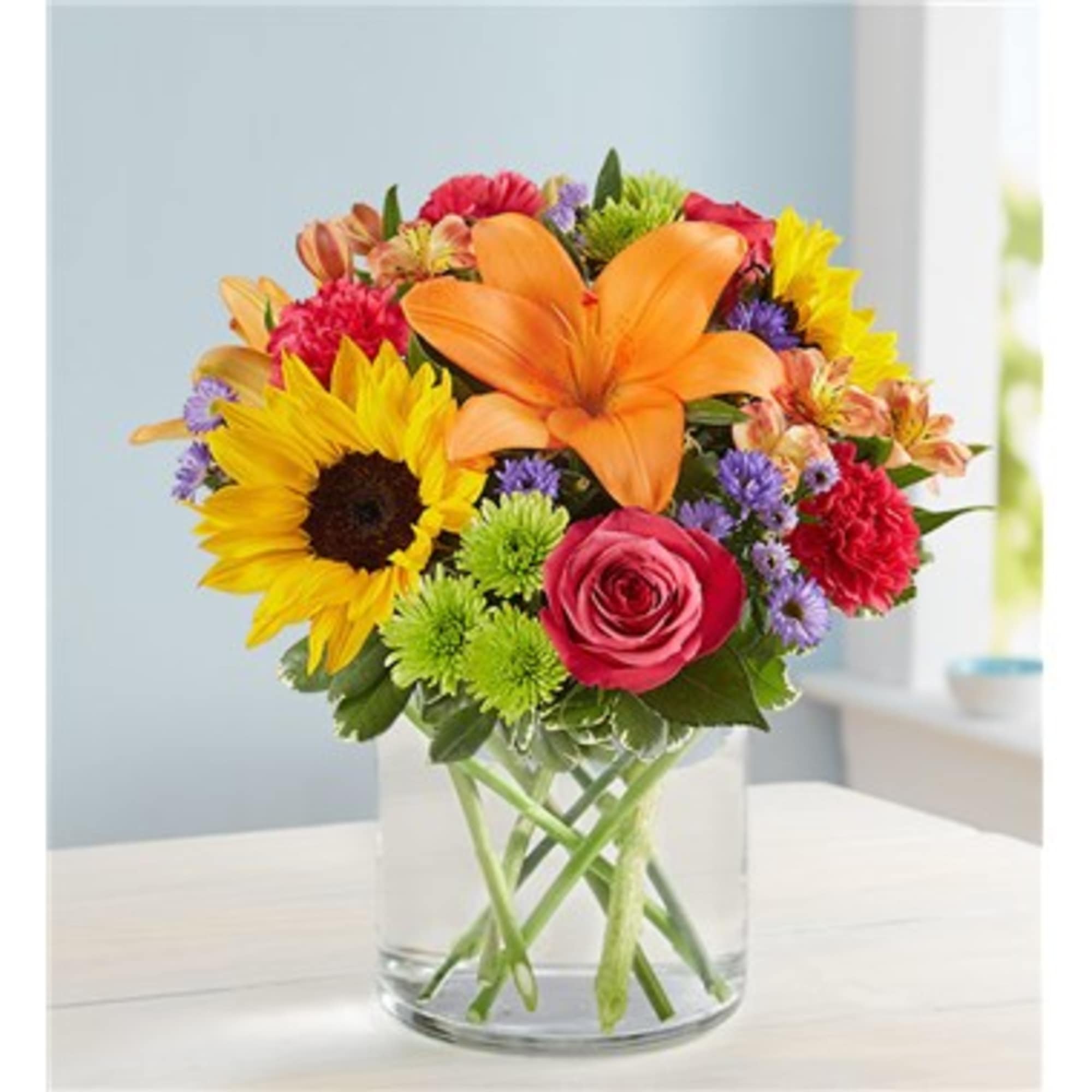 Colorful mixed bouquet in a clear glass vase with sunflower, lily, and rose blooms