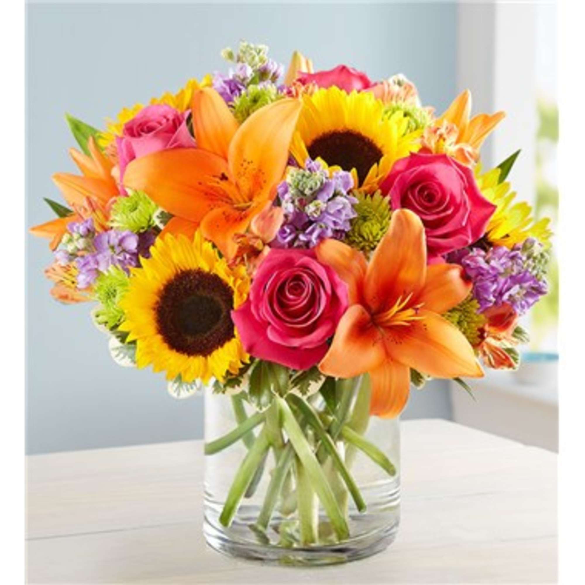 Bright mixed bouquet of sunflowers, roses, and orange lilies in a clear glass vase