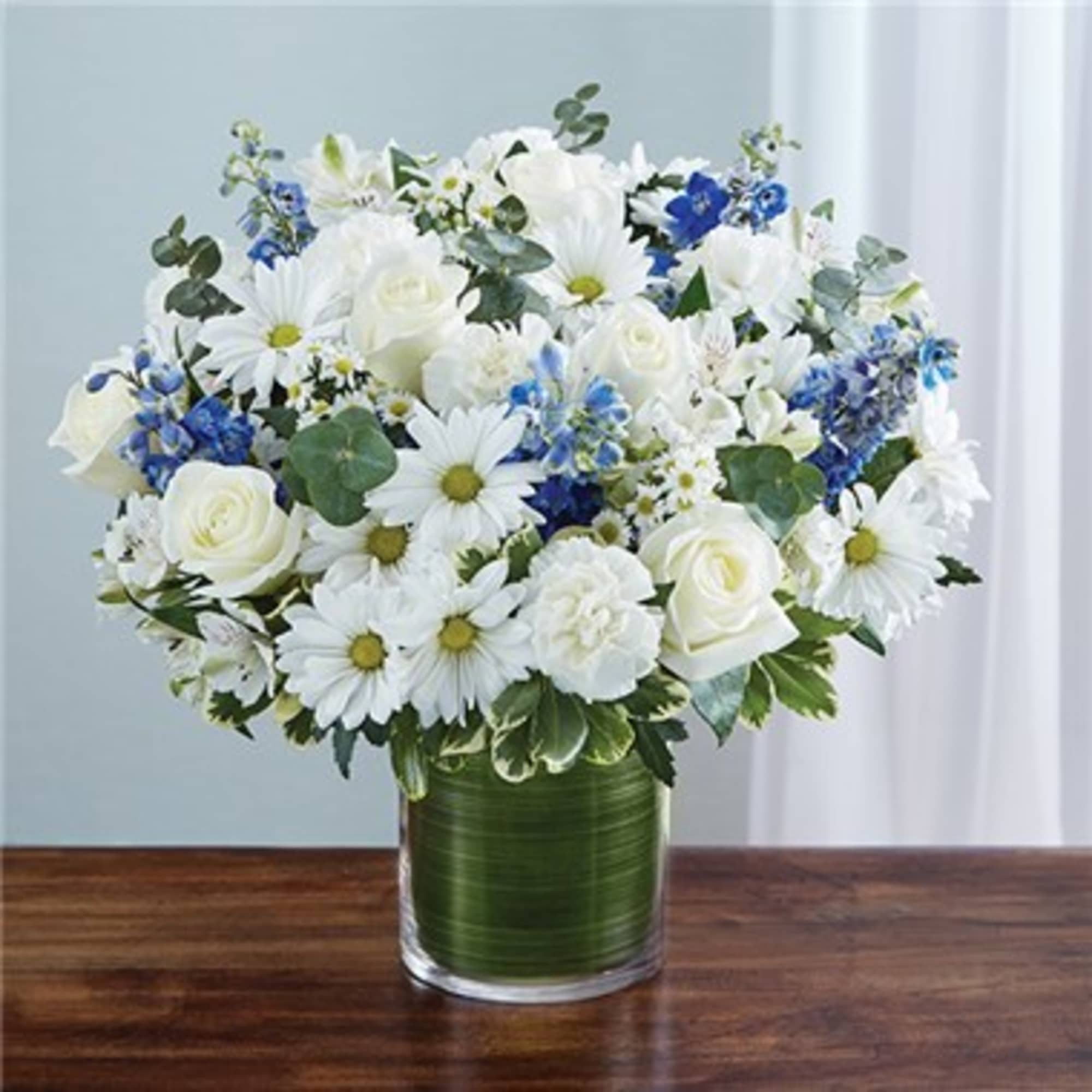 White daisies, roses, and blue flowers in a glass vase