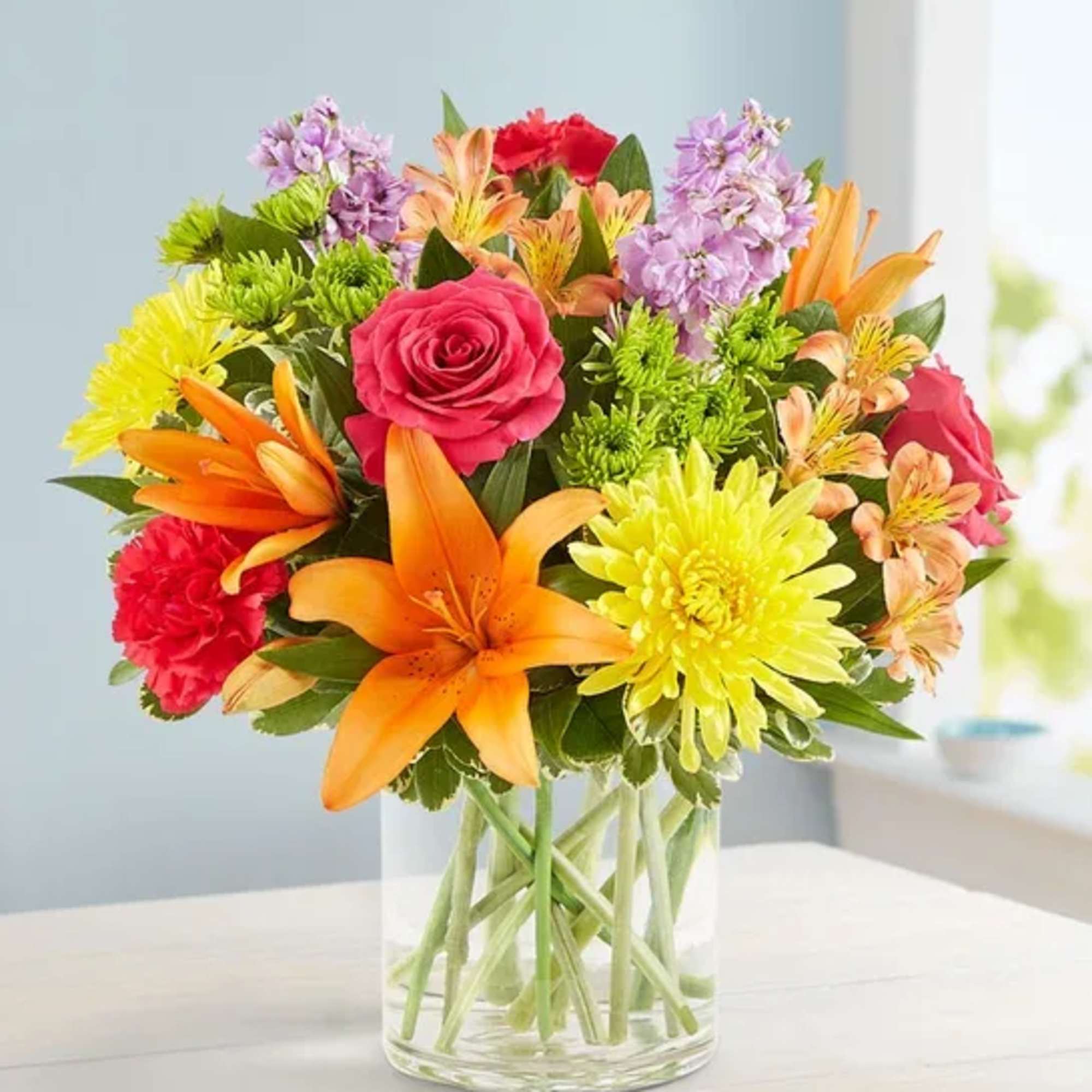 Colorful bouquet of roses, lilies, and chrysanthemums in a clear glass vase
