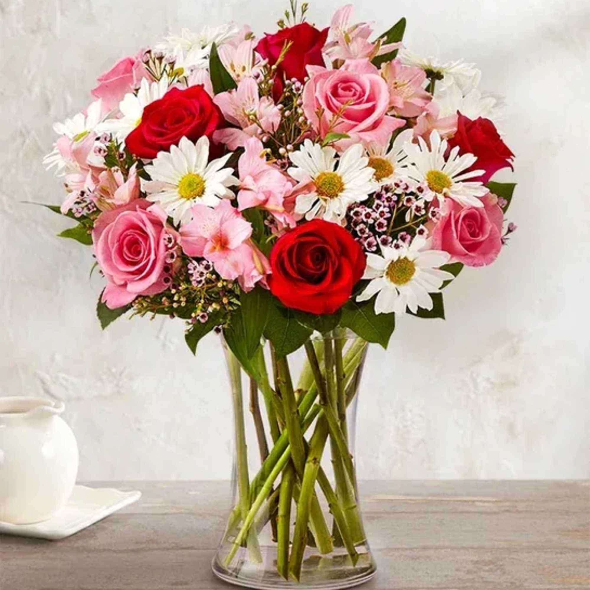 Bouquet of red and pink roses with white daisies in a clear glass vase