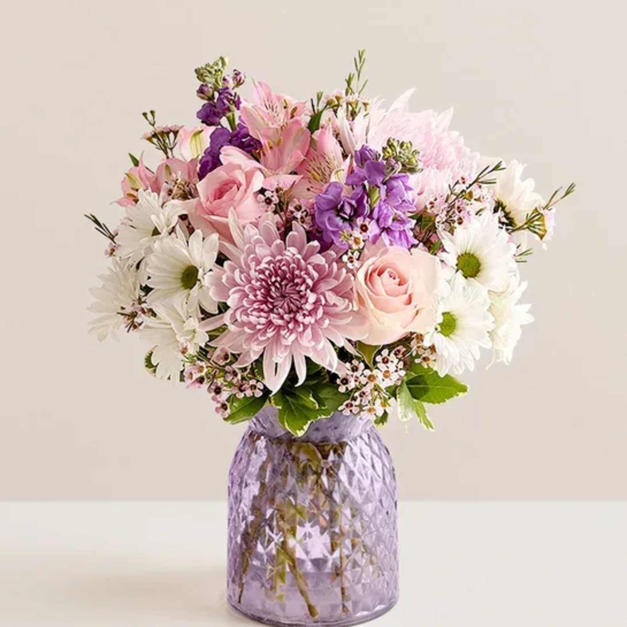 Pastel bouquet of pink roses, mums, daisies and purple blooms in a lavender glass vase