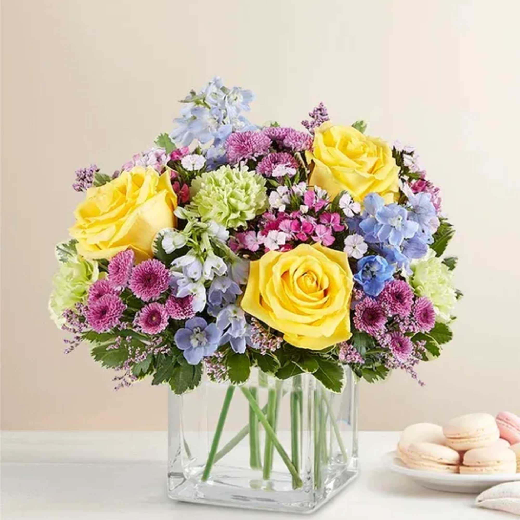 Yellow roses and pastel mixed flowers in a clear square vase