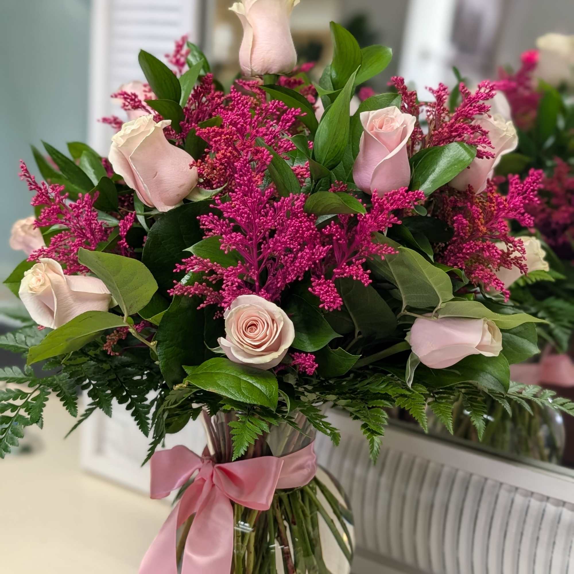Pink roses and magenta filler flowers in a glass vase with a pink ribbon