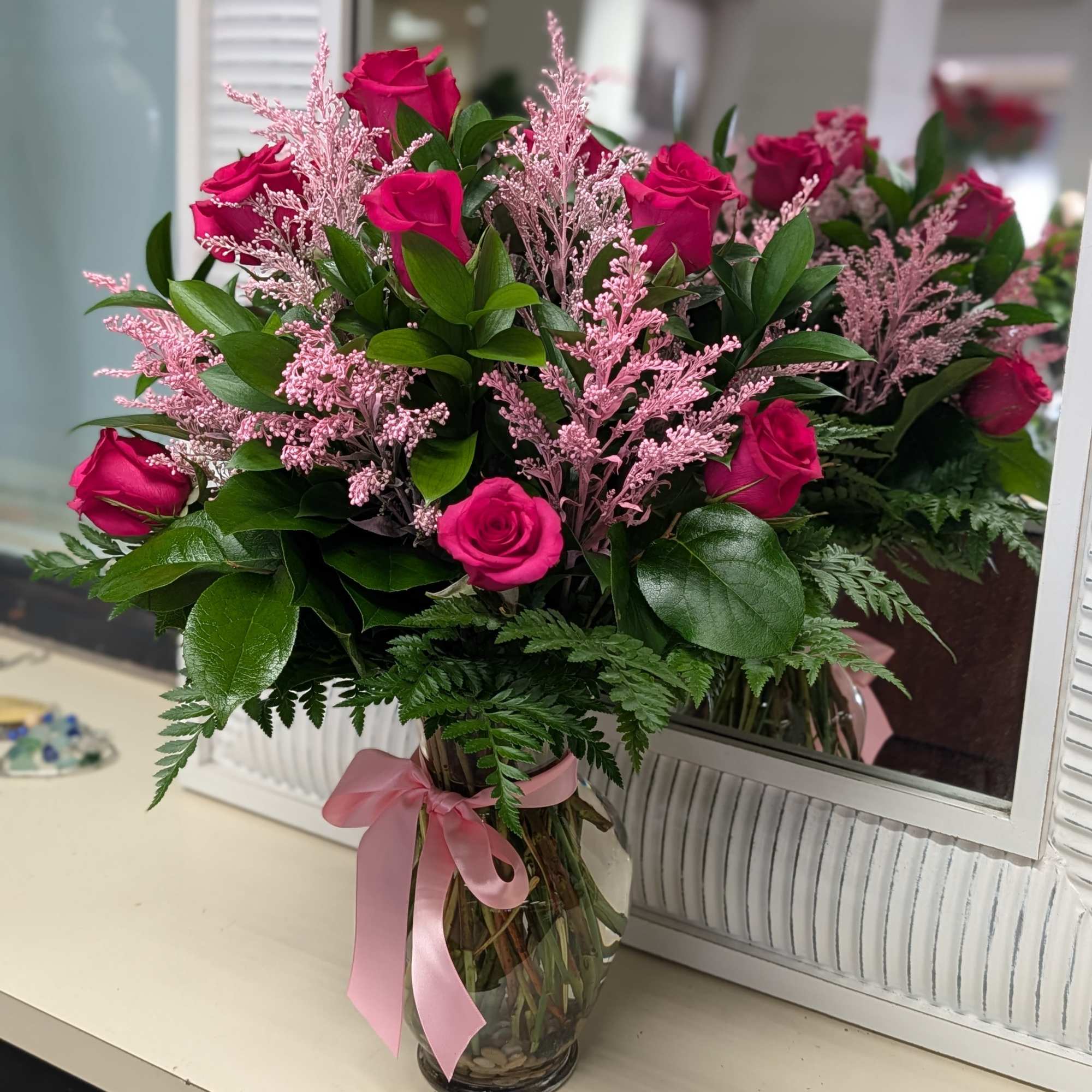 Arrangement of hot pink roses with pink filler in a clear glass vase tied with a pink ribbon
