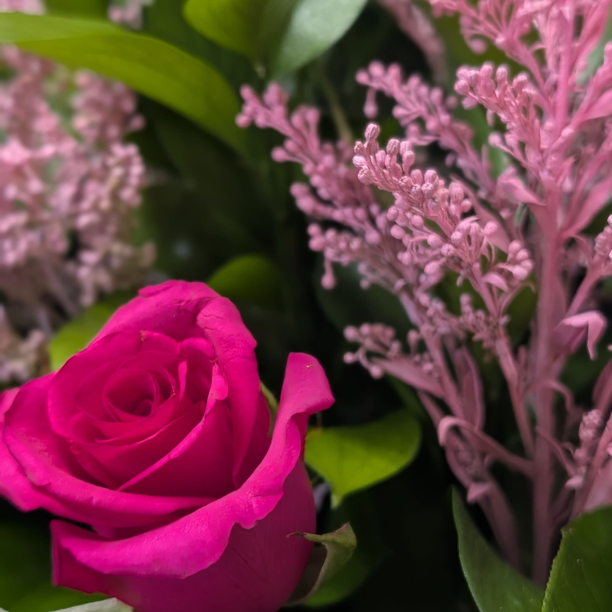 Close-up of a hot pink rose with soft pink filler blooms in a lush arrangement.