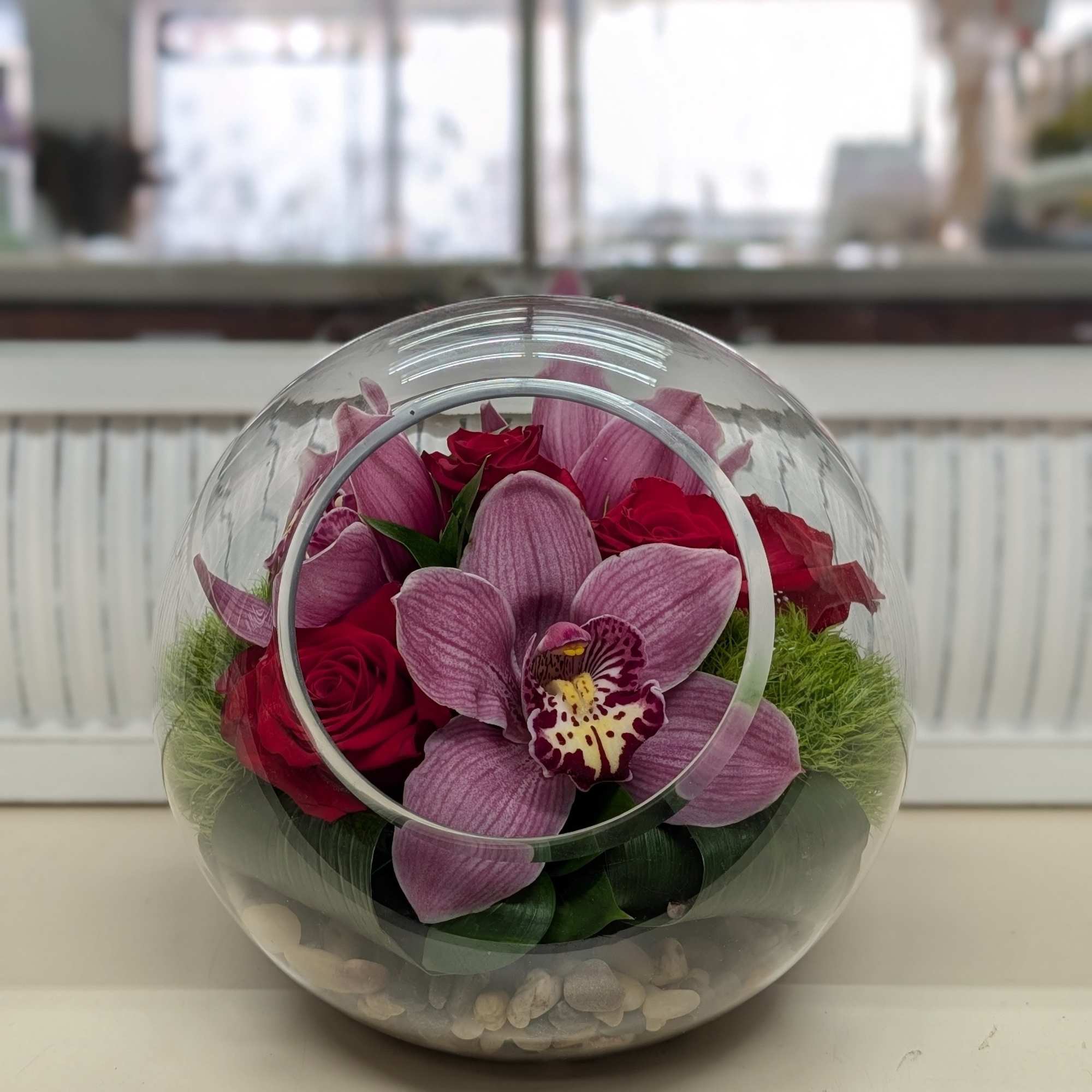 Pink orchids and red roses in a clear round glass vase